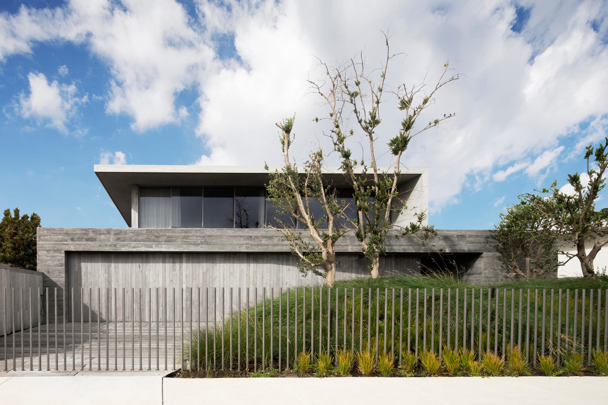 Silver Linings by Rachcoff Vella Architecture. Photography by Tatjana Plitt. Street facade of contemporary multi storey concrete residential home with modern metal fence and native garden beds. 