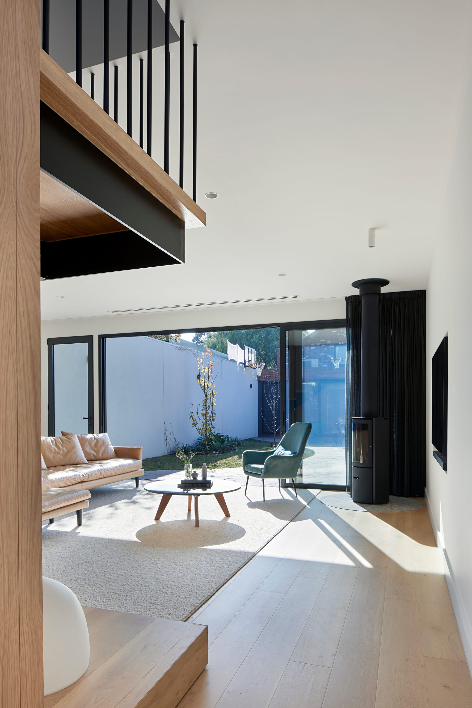 HMAS L02 by Rachcoff Vella Architecture. Photography by Tatjana Plitt. Living space with double height ceilings, mezzanine level in foreground and views over courtyard in background. 