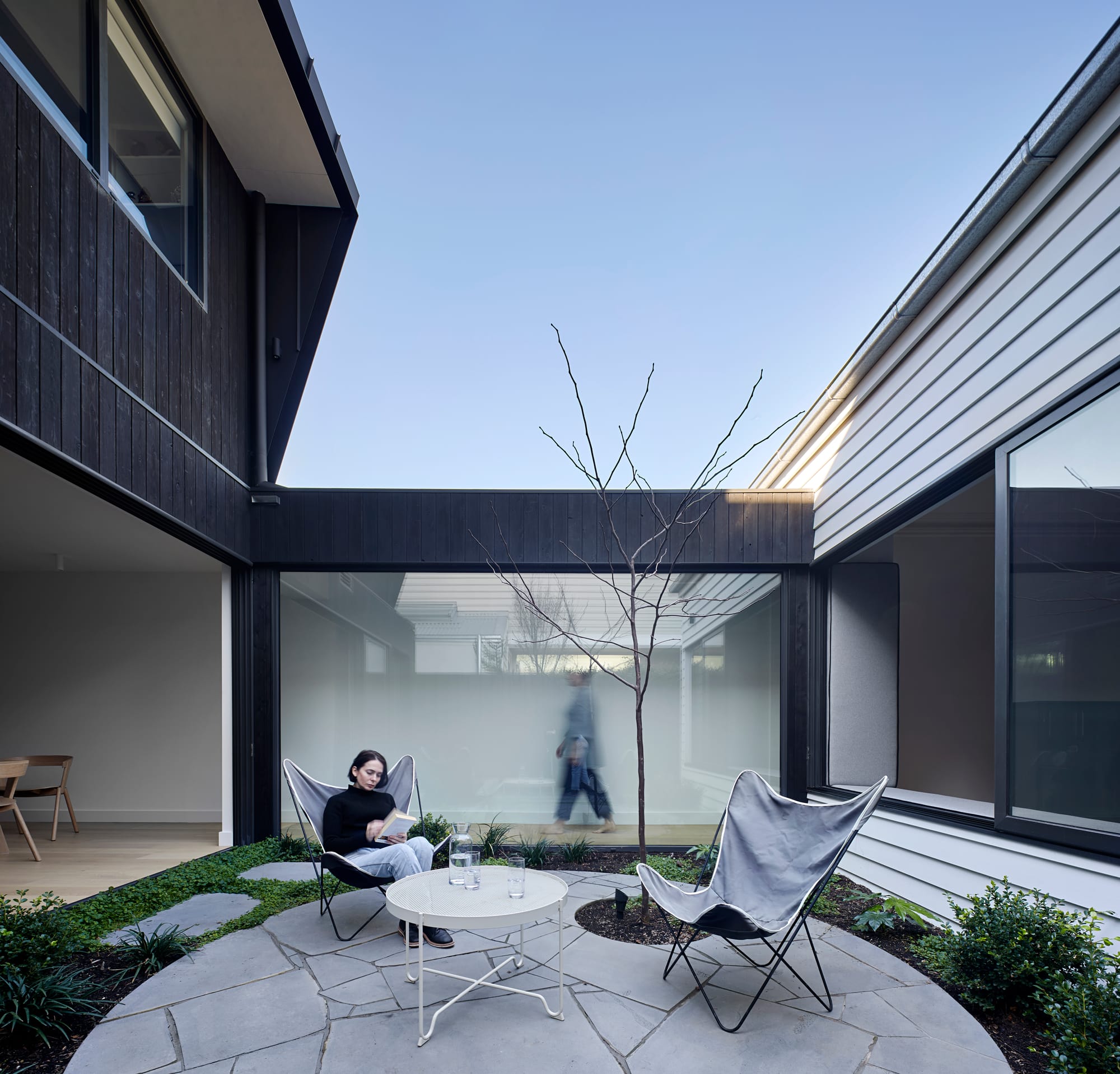 HMAS L02 by Rachcoff Vella Architecture. Photography by Tatjana Plitt. Paved interior courtyard space with glass interior walkway in background and charred black timber walls. 