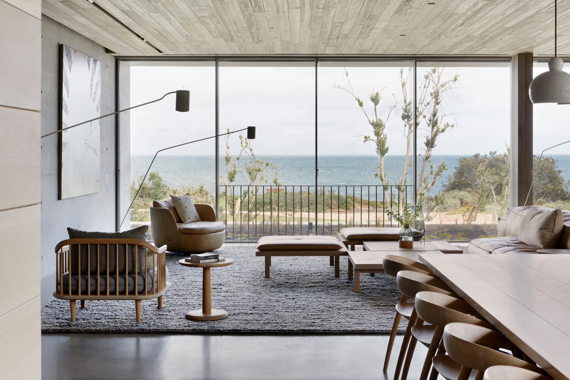 Silver Linings by Rachcoff Vella Architecture. Photography by Tatjana Plitt. Floor to cieling glass windows overlook coastal landscape in contemporary living space with mid-century modern inspired timber furniture. 