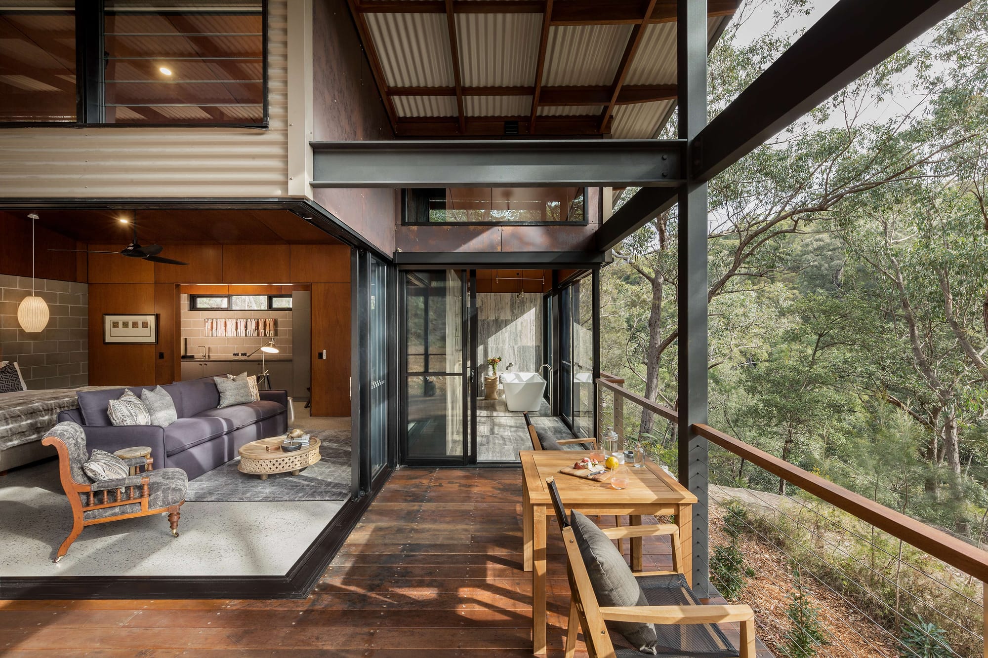 Spicers Sangoma by Barbara Tarnawski Architects. Bedroom suite with purple couch opening onto timber deck, overlooking bushland and ensuite in background. 