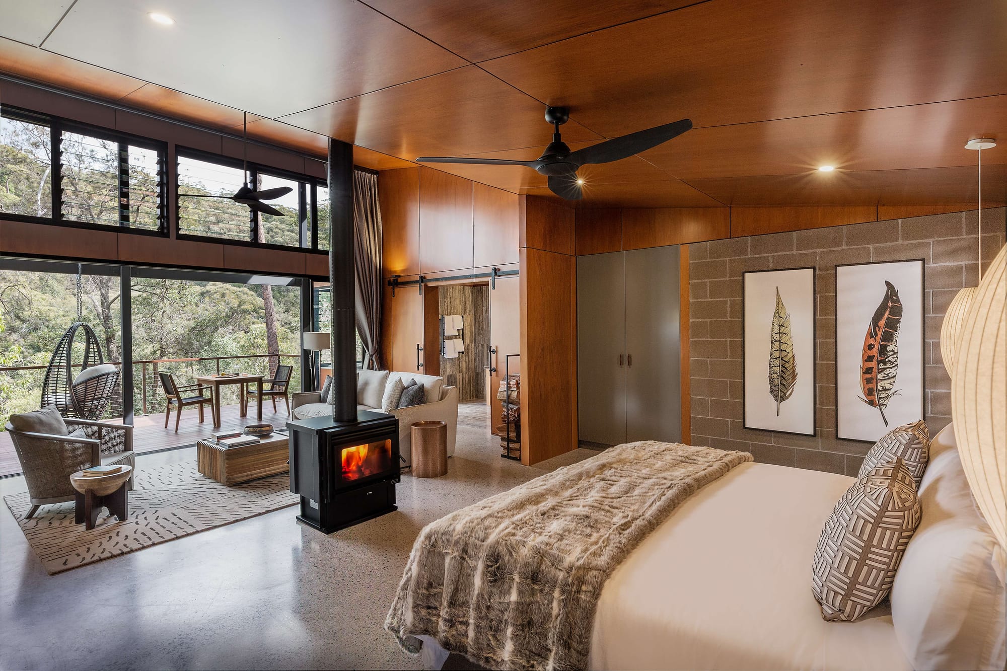 Spicers Sangoma by Barbara Tarnawski Architects. Bedroom suite with central fireplace, slanted timber ceilings, concrete floors and large white bed. 