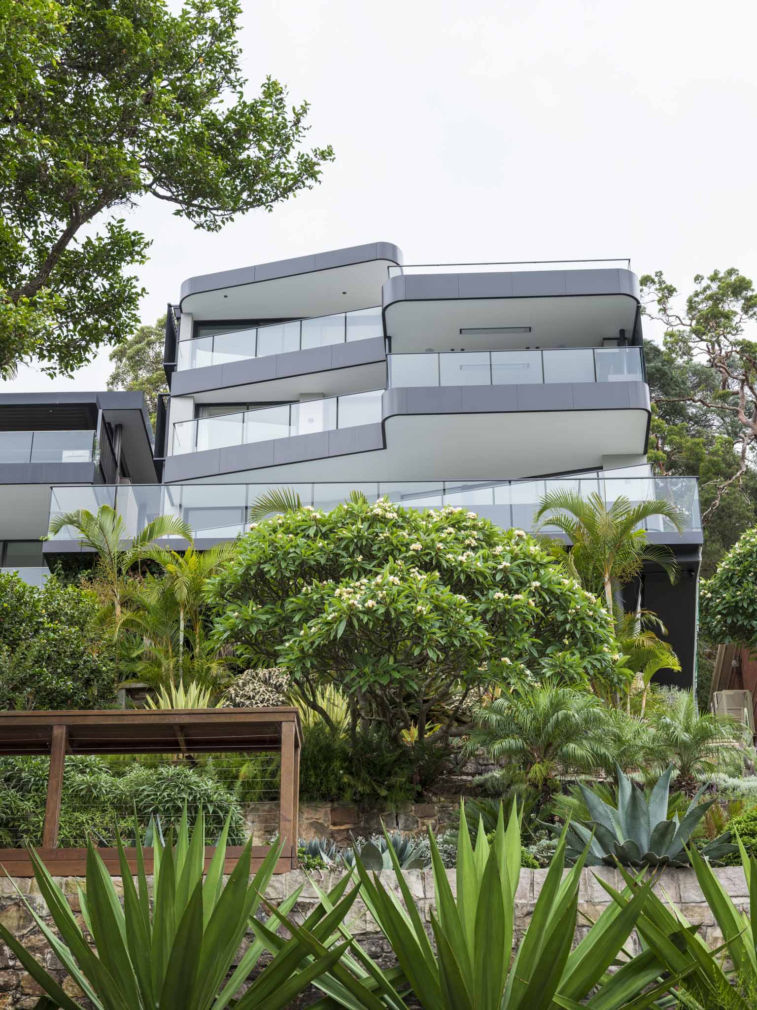 Sailors Bay by Castlepeake Architects. Photography by Tom Ferguson. Rear facade of home from low angle, displaying the stacked balconies and levels of the home, with black steel and glass fencing.