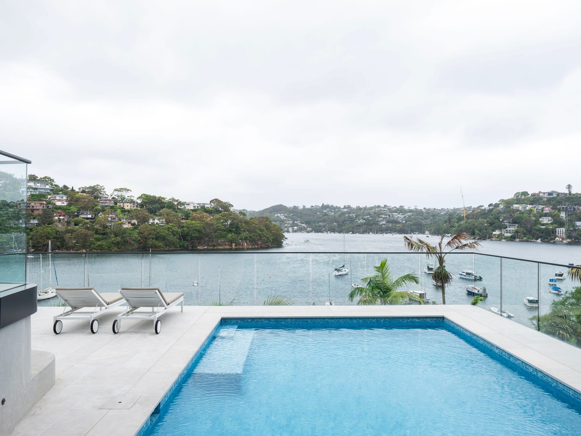 Sailors Bay by Castlepeake Architects. Photography by Tom Ferguson. Pool on balcony overlooking harbour and hills, with grey tiles and glass fencing. 