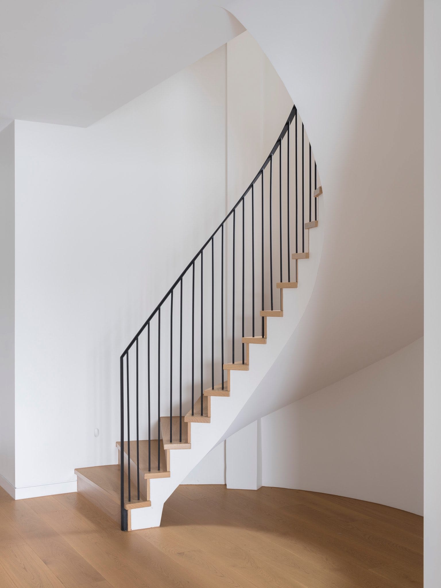 Sailors Bay by Castlepeake Architects. Photography by Tom Ferguson. White and timber spiral staircase with black balustrade in empty hallway with white walls and timber floors.