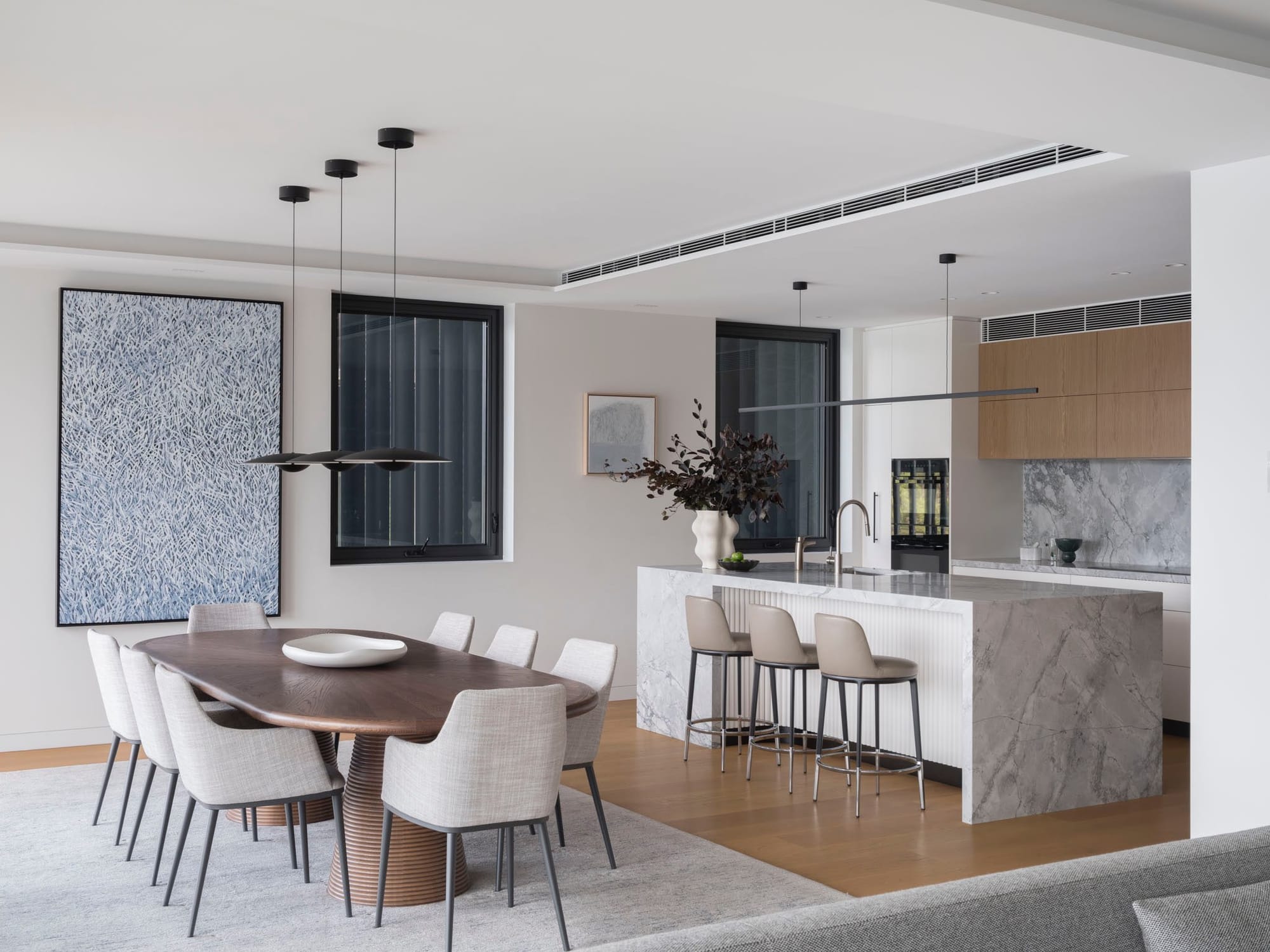 Sailors Bay by Castlepeake Architects. Photography by Tom Ferguson. Open plan kitchen and didning space with timber floors and white walls throughout, a dark timber curved dining table and black pendant lights.  dining space with 