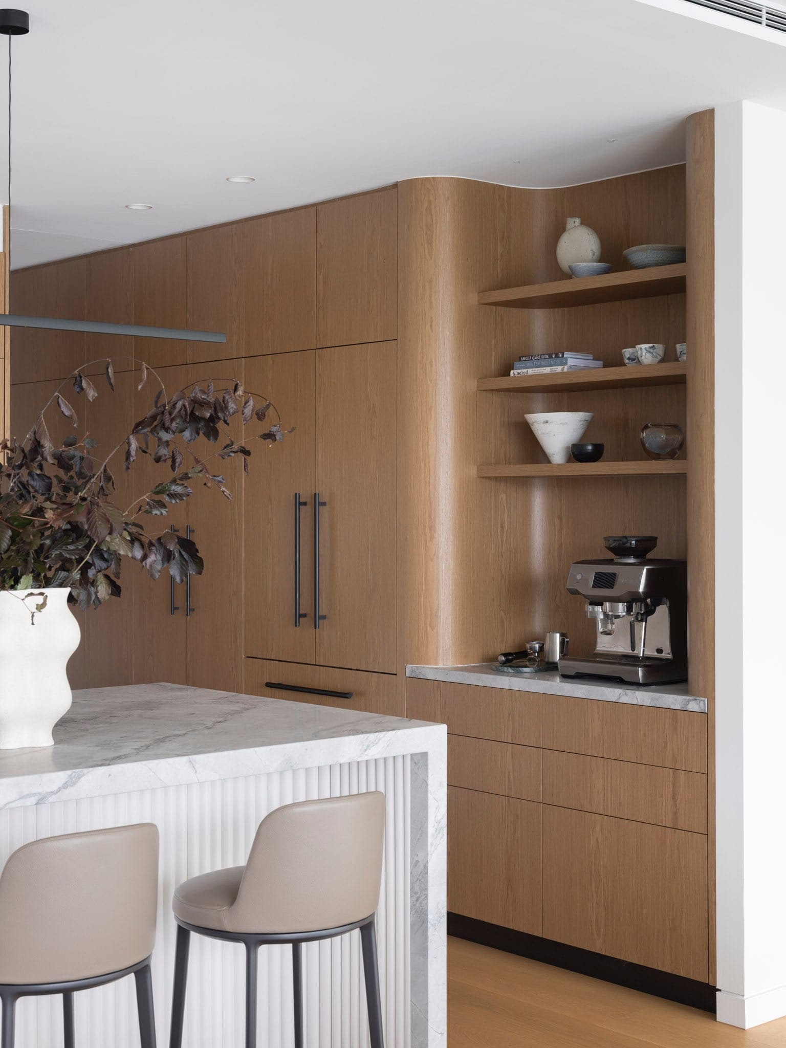 Sailors Bay by Castlepeake Architects. Photography by Tom Ferguson. Kitchen with timber joinery and marble island bench with leather chairs and fluted kickboard. 