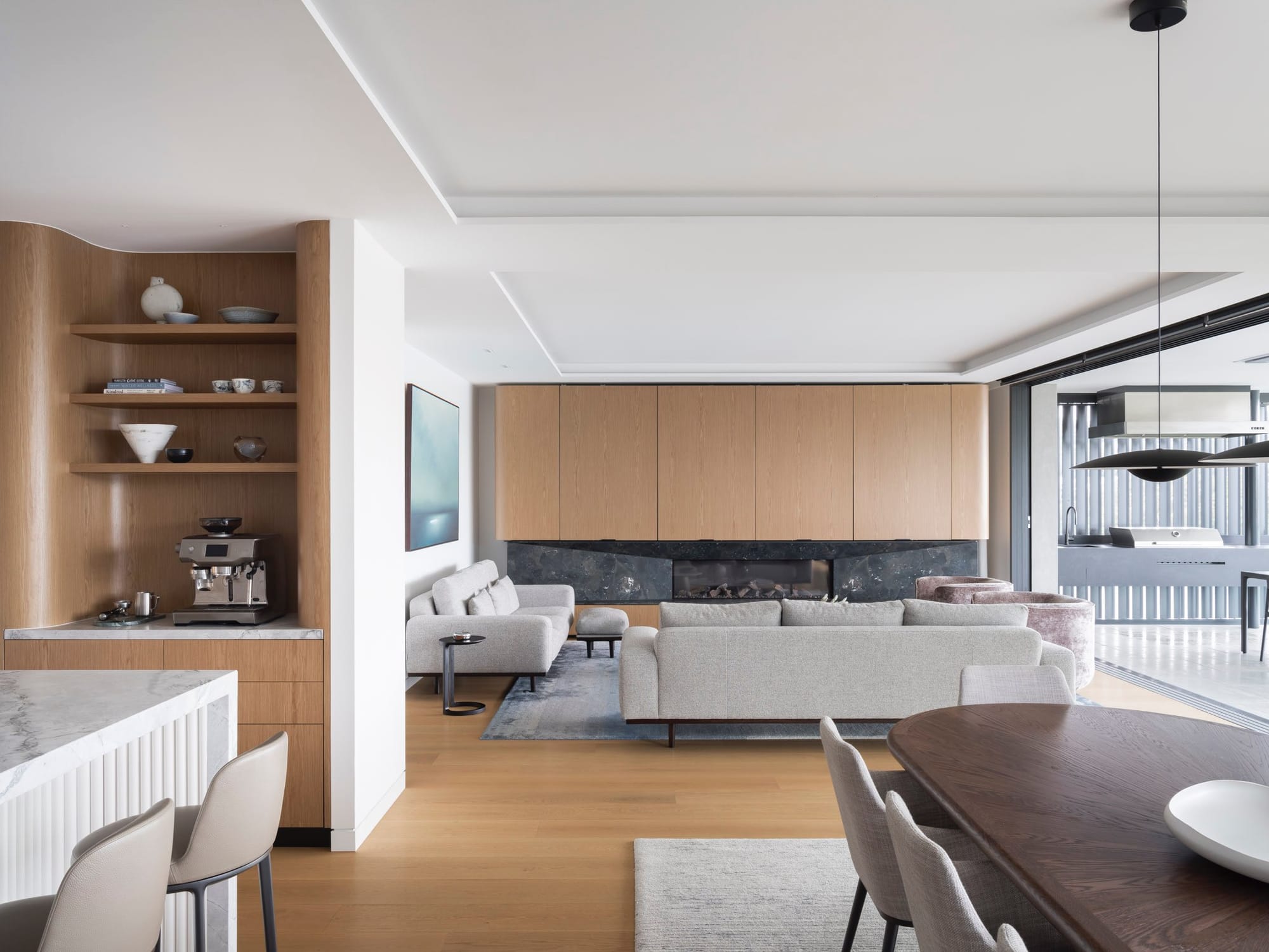 Sailors Bay by Castlepeake Architects. Photography by Tom Ferguson. Open plan kitchen, living and dining space with timber joinery and flooring throughout, white ceilings and beige linen chairs and carpets. 