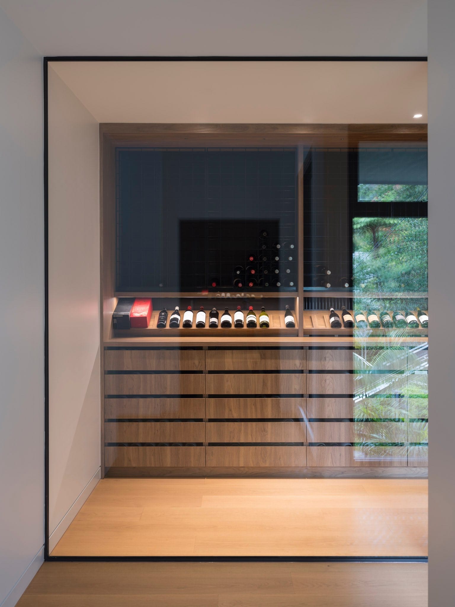 Sailors Bay by Castlepeake Architects. Photography by Tom Ferguson. Timber cellar storage with many wine bottles behind glass cellar door with timber floors and white walls. 