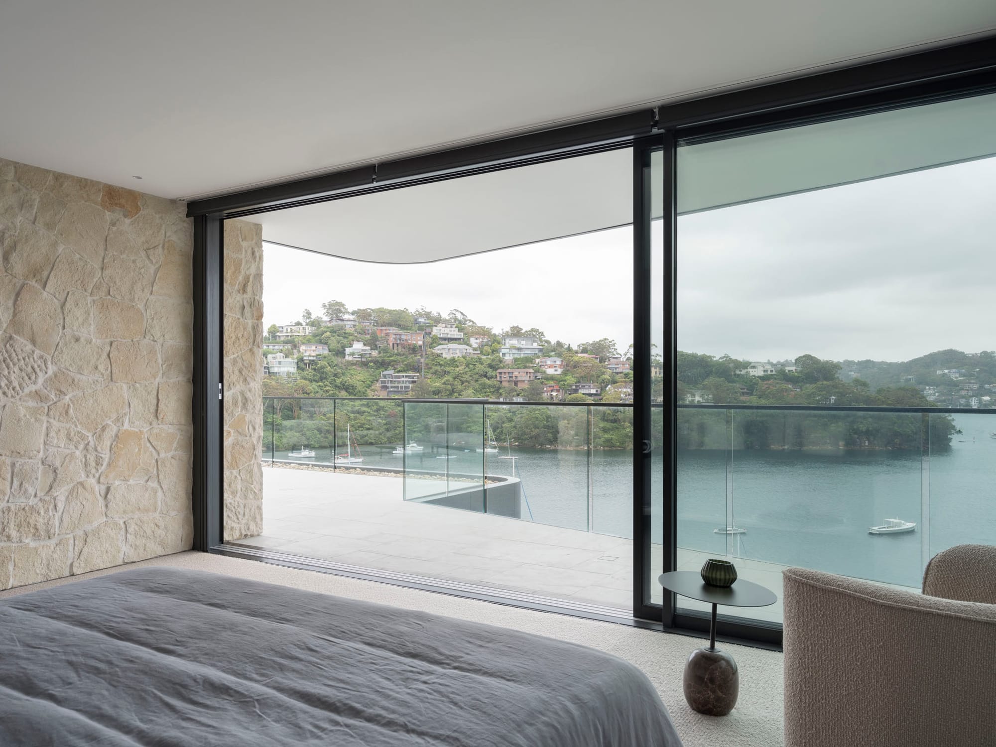 Sailors Bay by Castlepeake Architects. Photography by Tom Ferguson. Views over harbour and hillside from upper level bedroom and adjoining balcony, with floor-to-ceiling glass sliding windows, doors and fencing. 