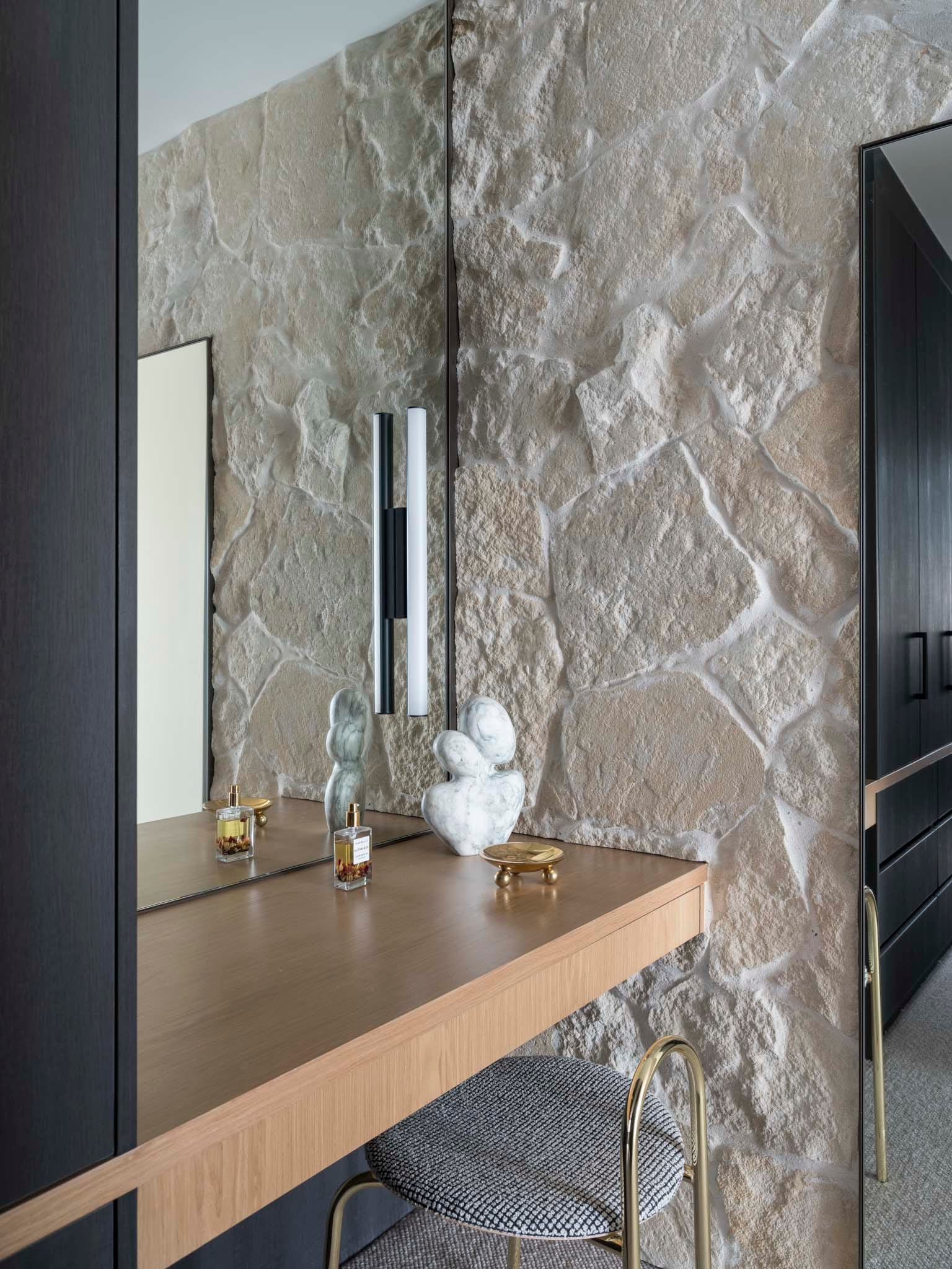 Sailors Bay by Castlepeake Architects. Photography by Tom Ferguson. Sandstone feature wall next to integrated dressing table with large mirror, timber floating benchtop and black cabinetry surrounds. 