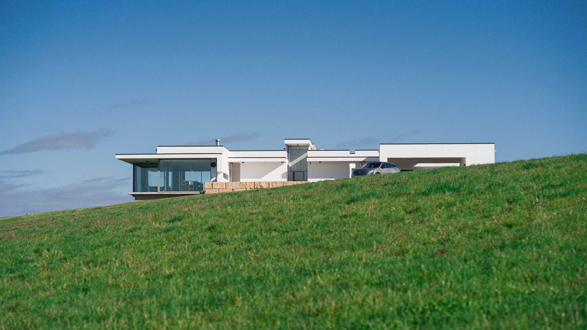 The Cloud at Sen Vineyard. Photography by Ben Little. Enclosed courtyard area with white gravel and firepit to left of contemporary white home at night, with warm light visible through full length glass walls. 