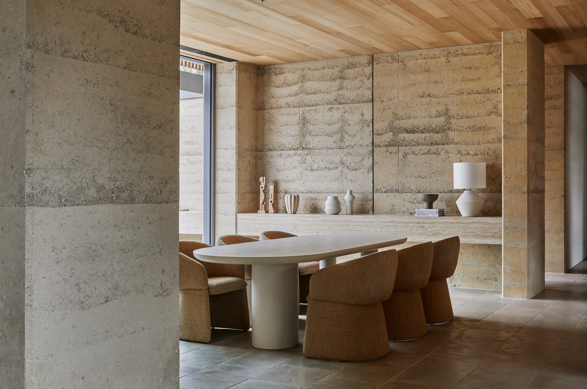 GlobeWest Volume 02 Collection 25. Dining table in room with rammed earth walls and brown curved chairs. 