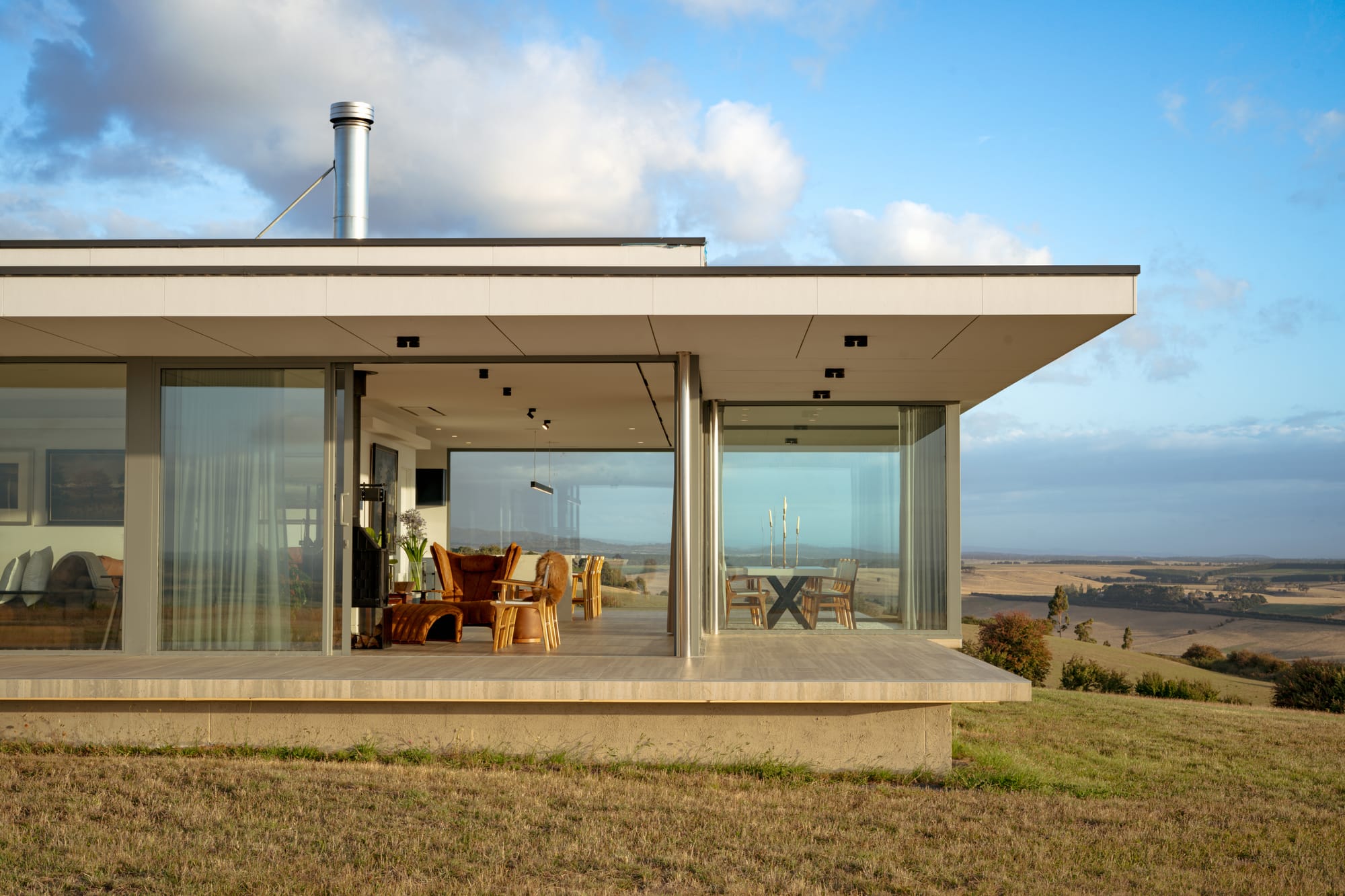 The Cloud at Sen Vineyard. Photography by Ben Little. Verandah and living space of holiday home with glass walls, stone flooring and modern furnishings. 