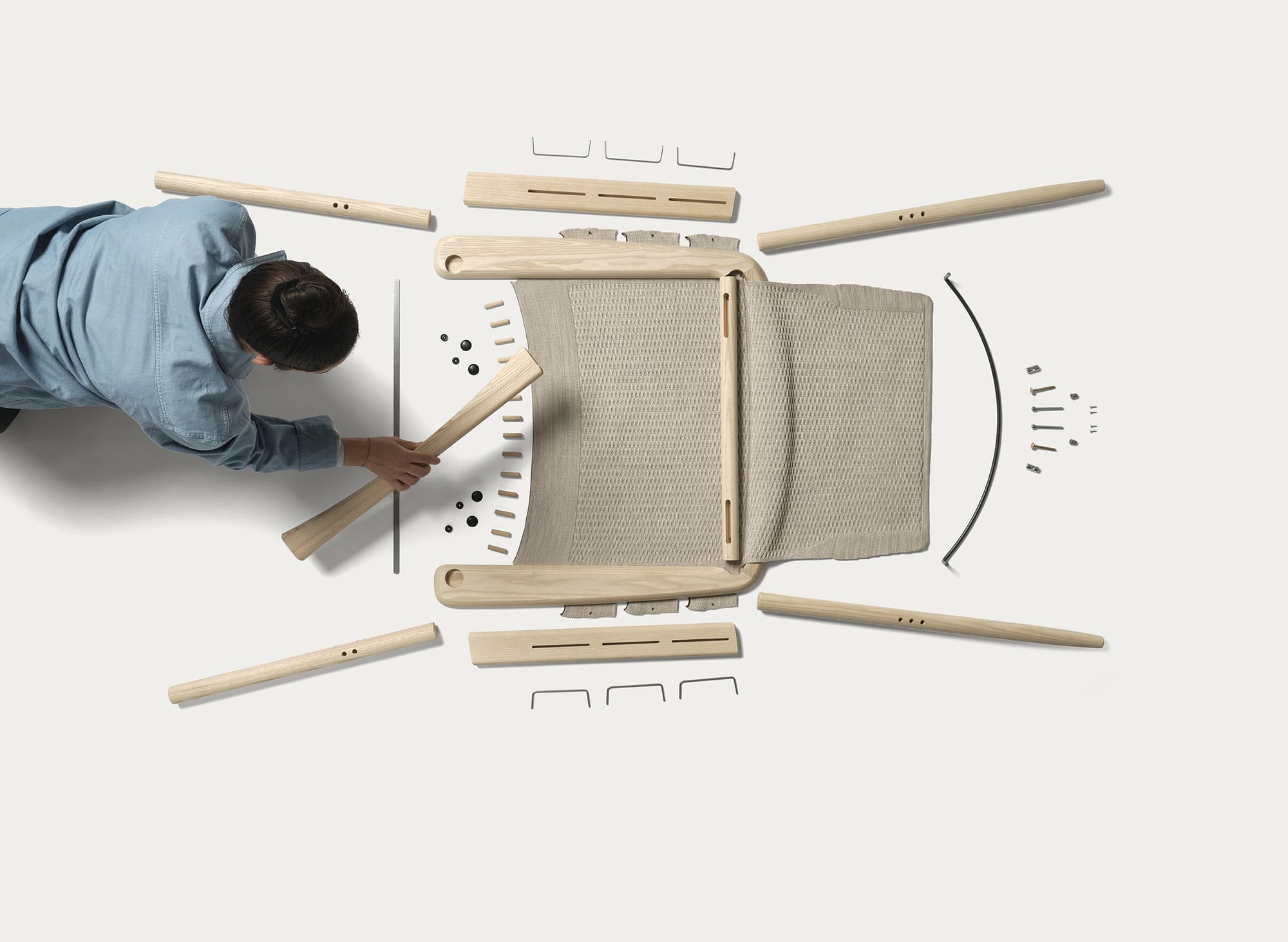 Evo Chair by EFG. Birds eye view of man constructing a timber and knit chair on a white background. 