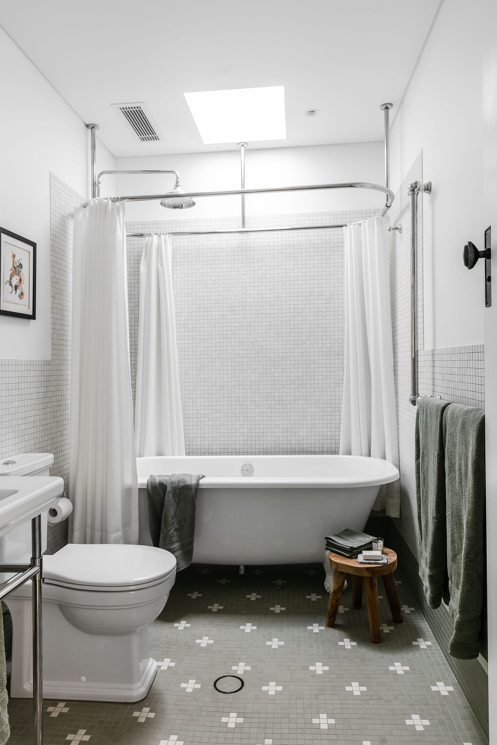 Interior of the country style bathroom with standalone bathtub and white and green tiles. Large skylight above.