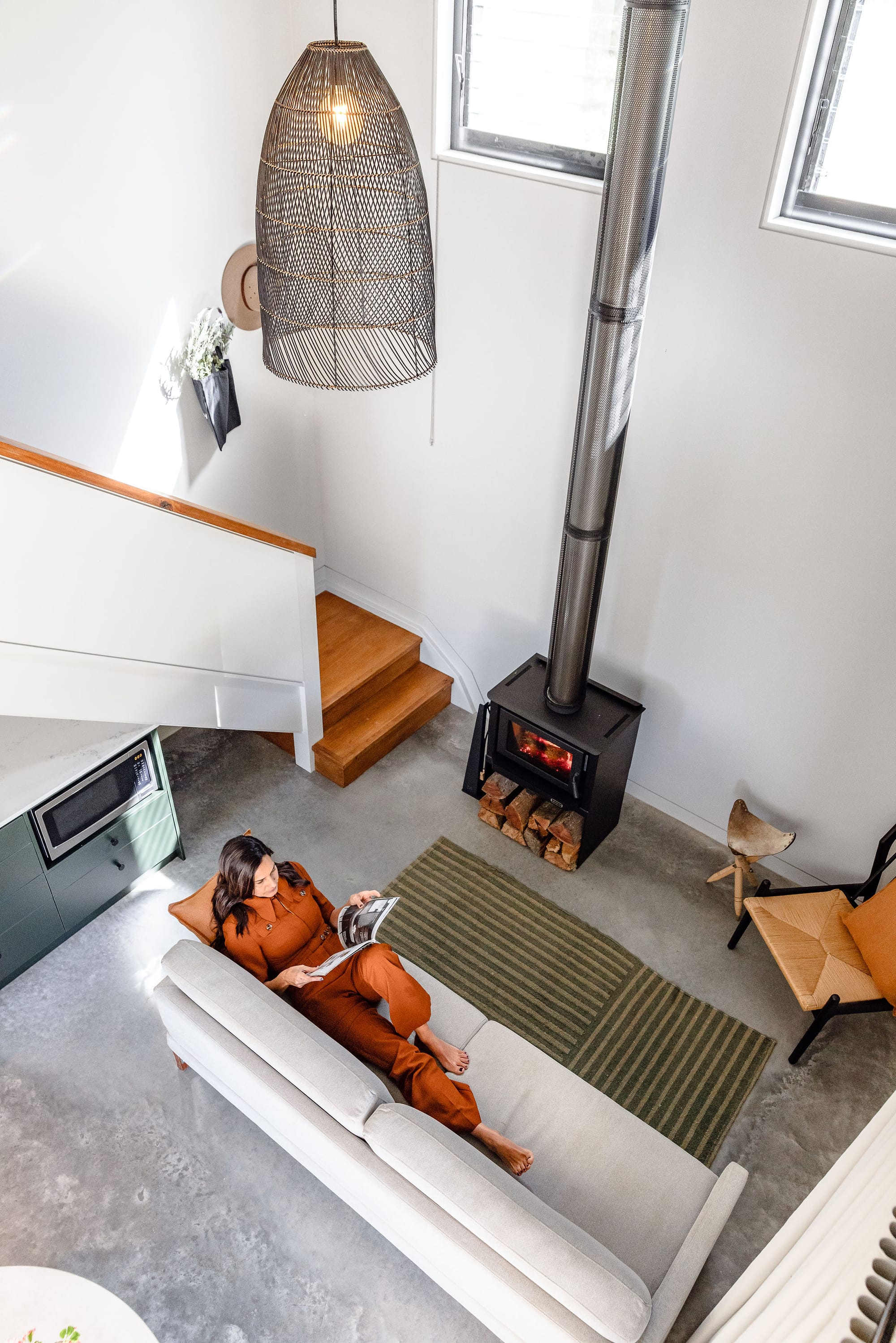 A shot from above showing Nido's interior with a woman laying on the sofa reading infront of the fireplace.