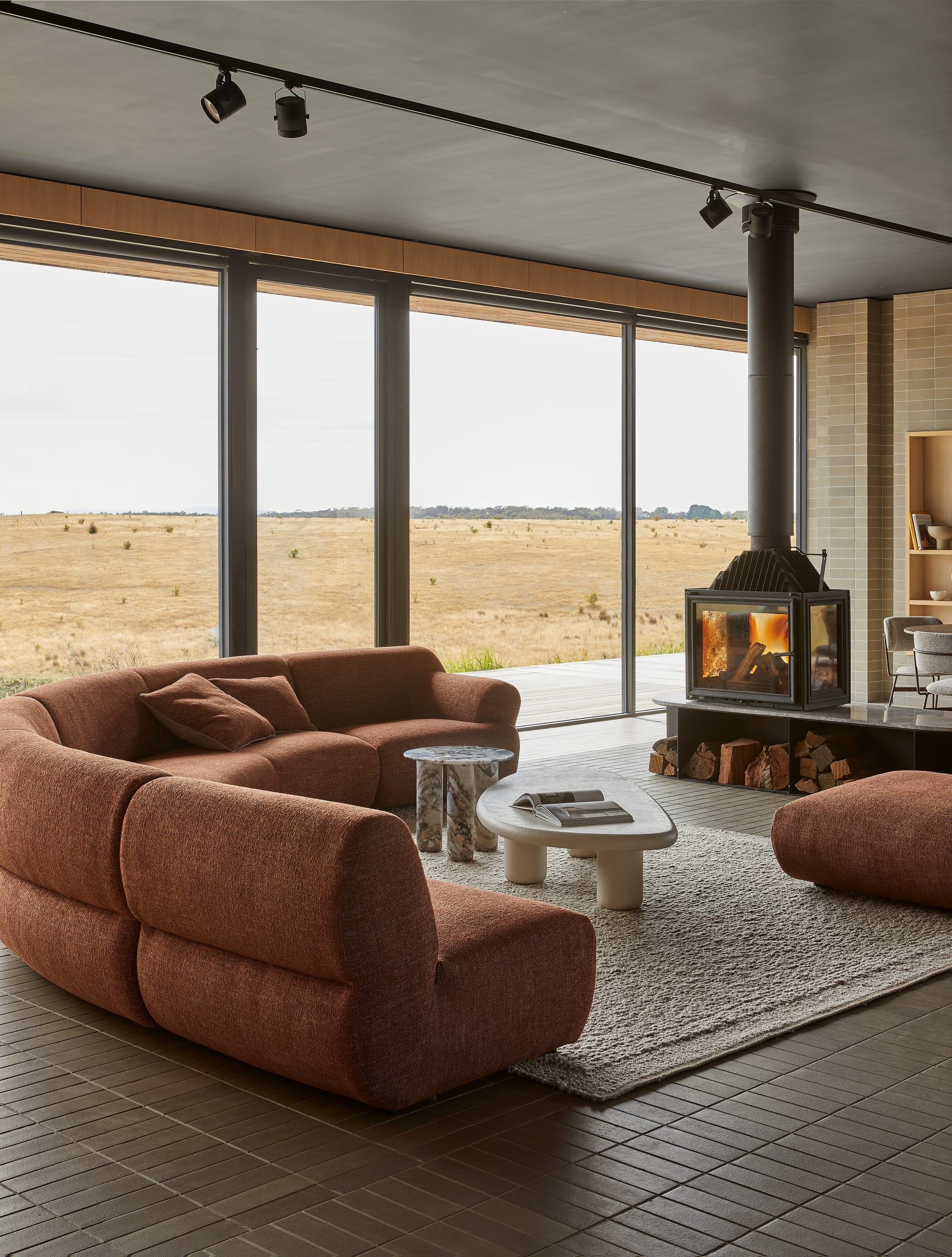 Juno Cloud by GlobeWest from Collection 2025.  Burnt orange modular rounded couch on tiled living room floor with fireplace and floor-to-ceiling windows.