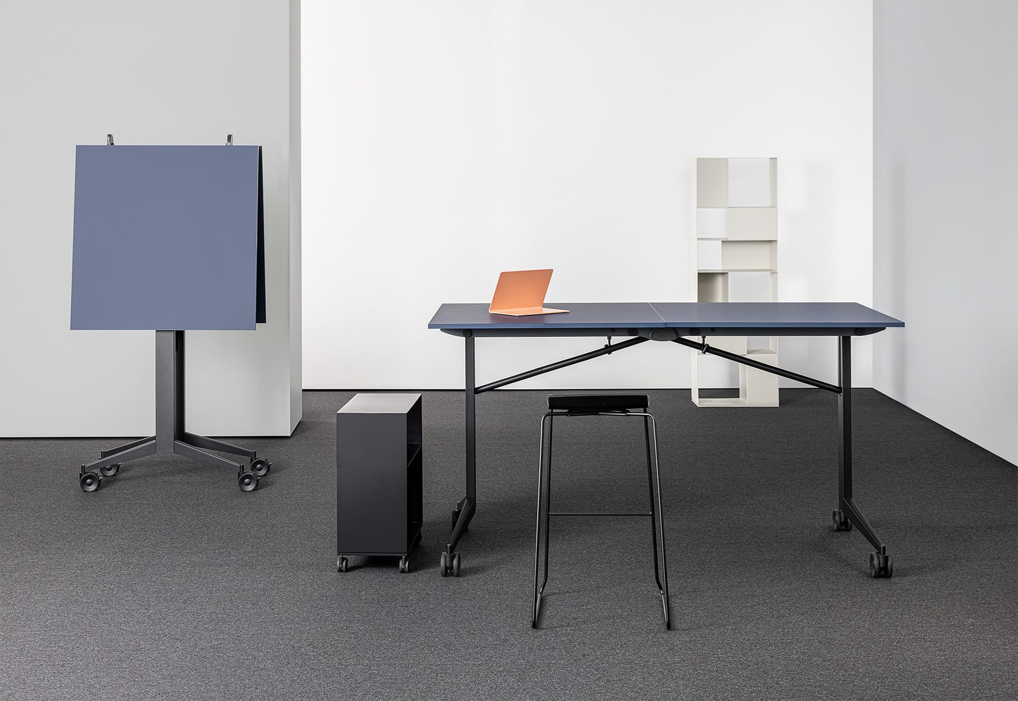 Libro Folding Table by Mara SRL. Blue office desk in office space with grey carpets and a black stool. 