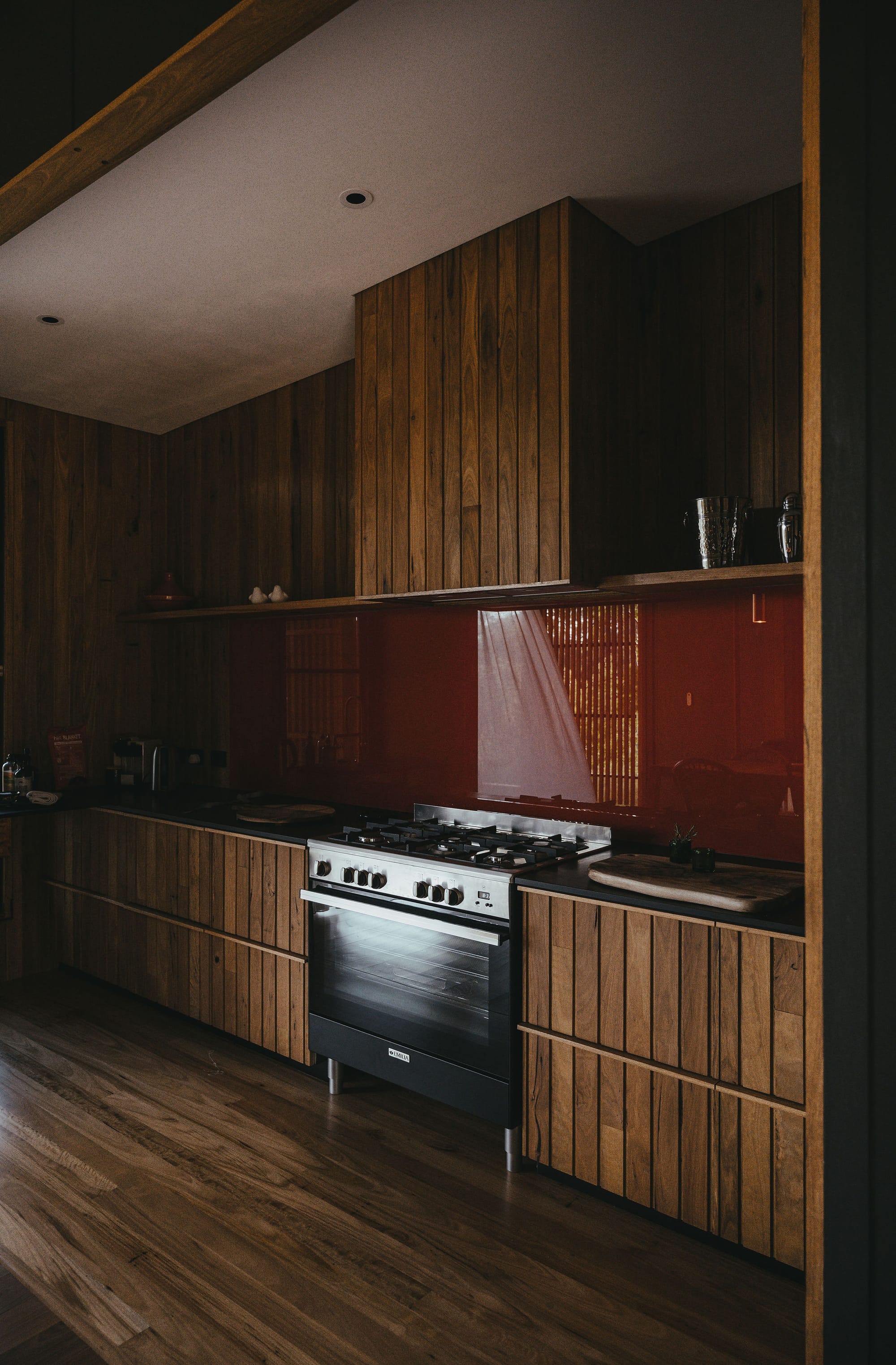 The Summer House at Little Valley Farm. Photography by Milou Hofman Photography. Open plan dining and kitchen space with timber floors and joinery, red splashback and mismatched dining chairs.