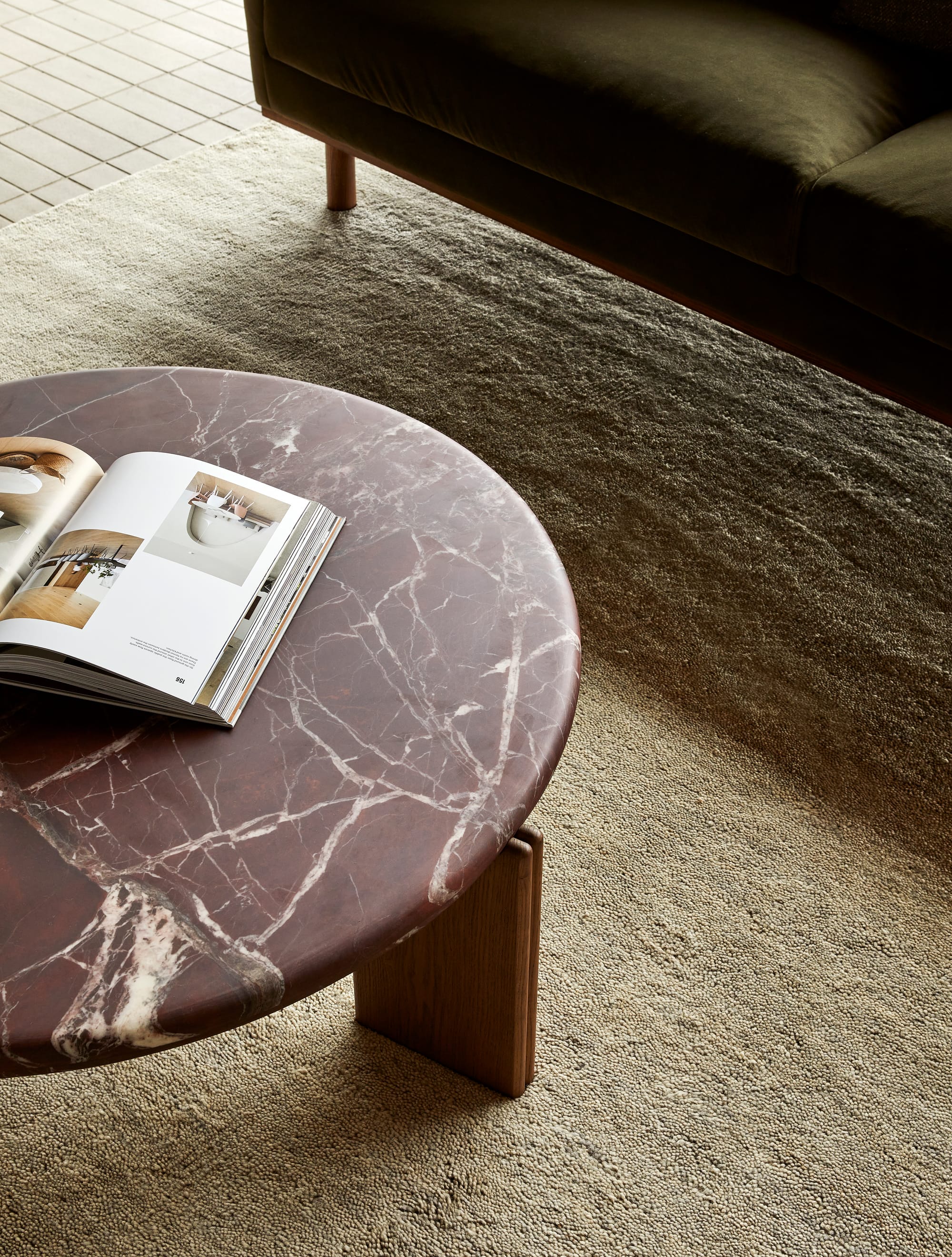 Ray by GlobeWest from Collection 2025. Half a brown marble coffee table on neutral carpet with timber legs and a magazine open on top.