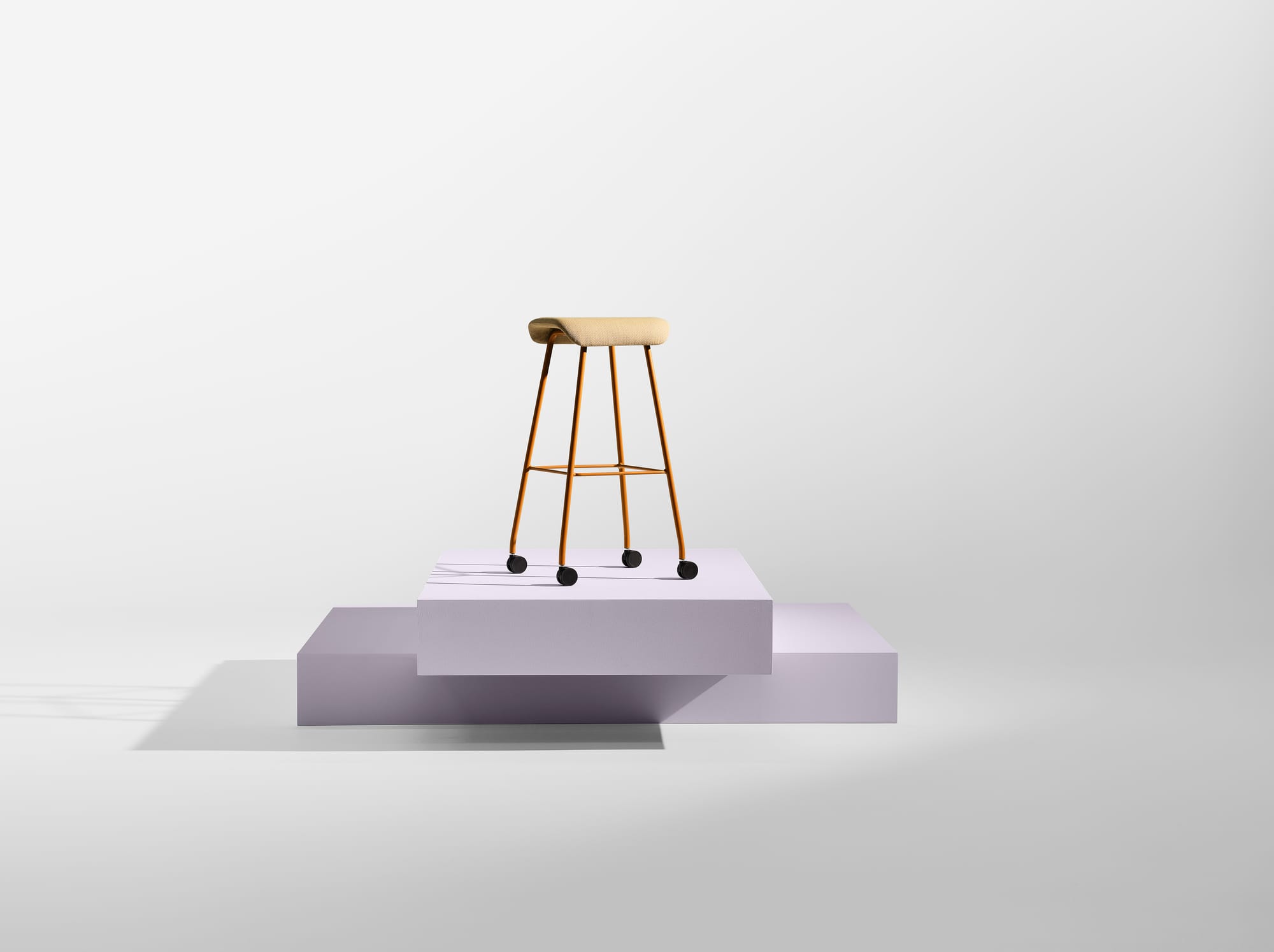 Sela Stool by EFG. Lilac podium in white space with single timber and tan stool with wheels on it. 