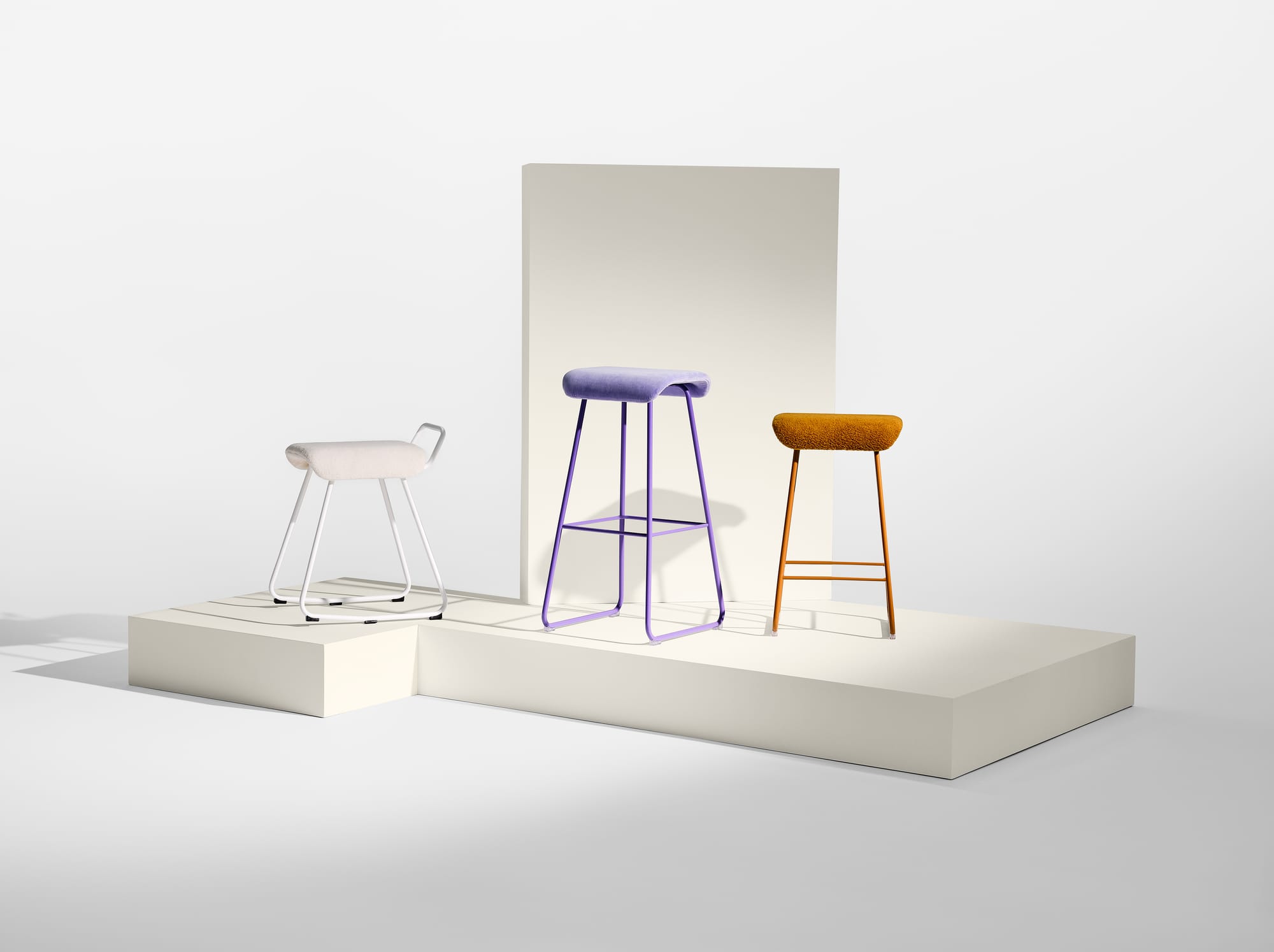 Sela Stool by EFG. Three stools in white, purple and orange arranged on white podium with white background. 