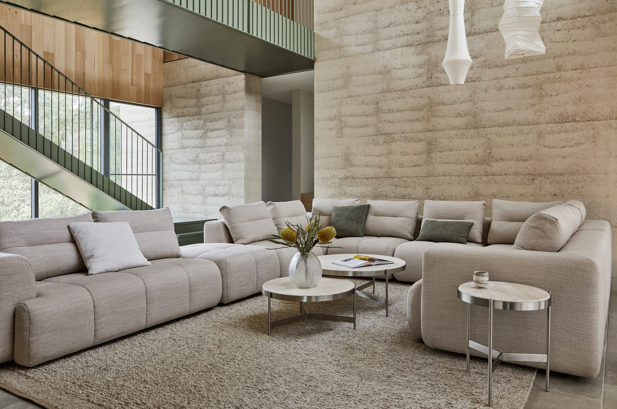 Sidney Tullio by GlobeWest from Collection 2025.  Grey modular lounge in double height open living space with pendant lighting and rammed earth walls. 