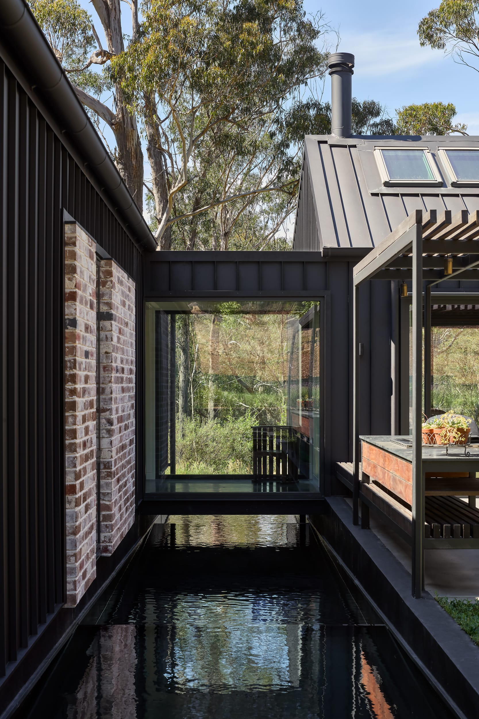 House Kimberley by AO Design Studio. Photography by Luc Remond. Glass walkway feature floating over water moat landscaping. Native Australian plant life visible in background through glass walkway. 