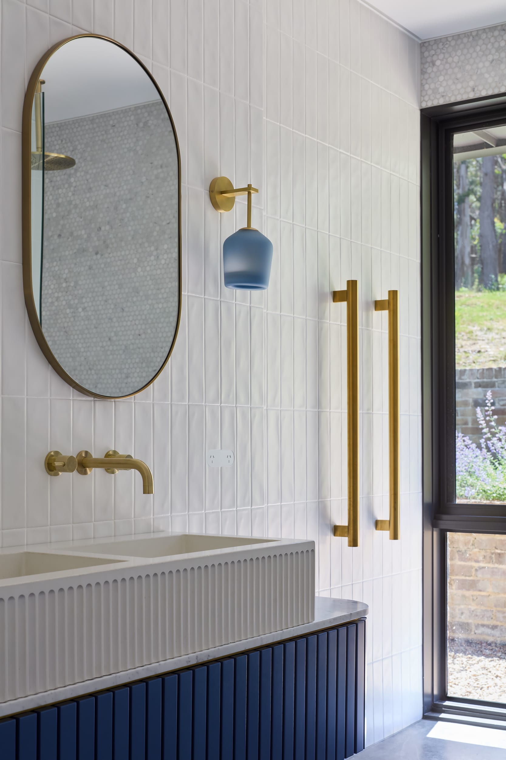 House Kimberley by AO Design Studio. Photography by Luc Remond. Bright and airy bathroom with electric blue timber console, white rectangular fluted double sink and gold tapware and feature hardware. 