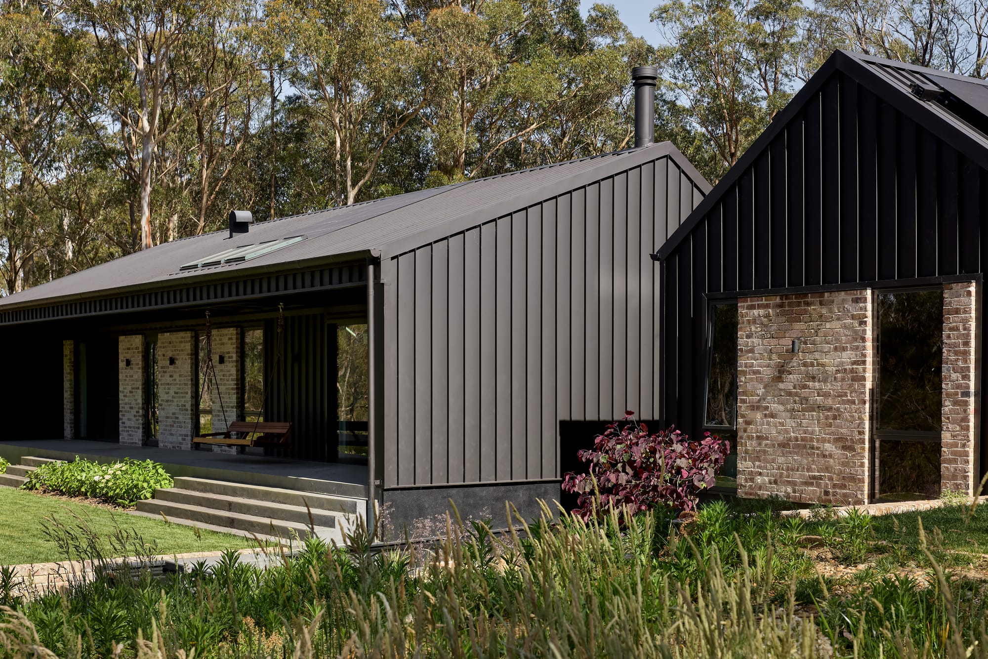 House Kimberley by AO Design Studio. Photography by Luc Remond. Black clad pavillion home with recycled brick wall accents, concrete steps and native grass garden. 