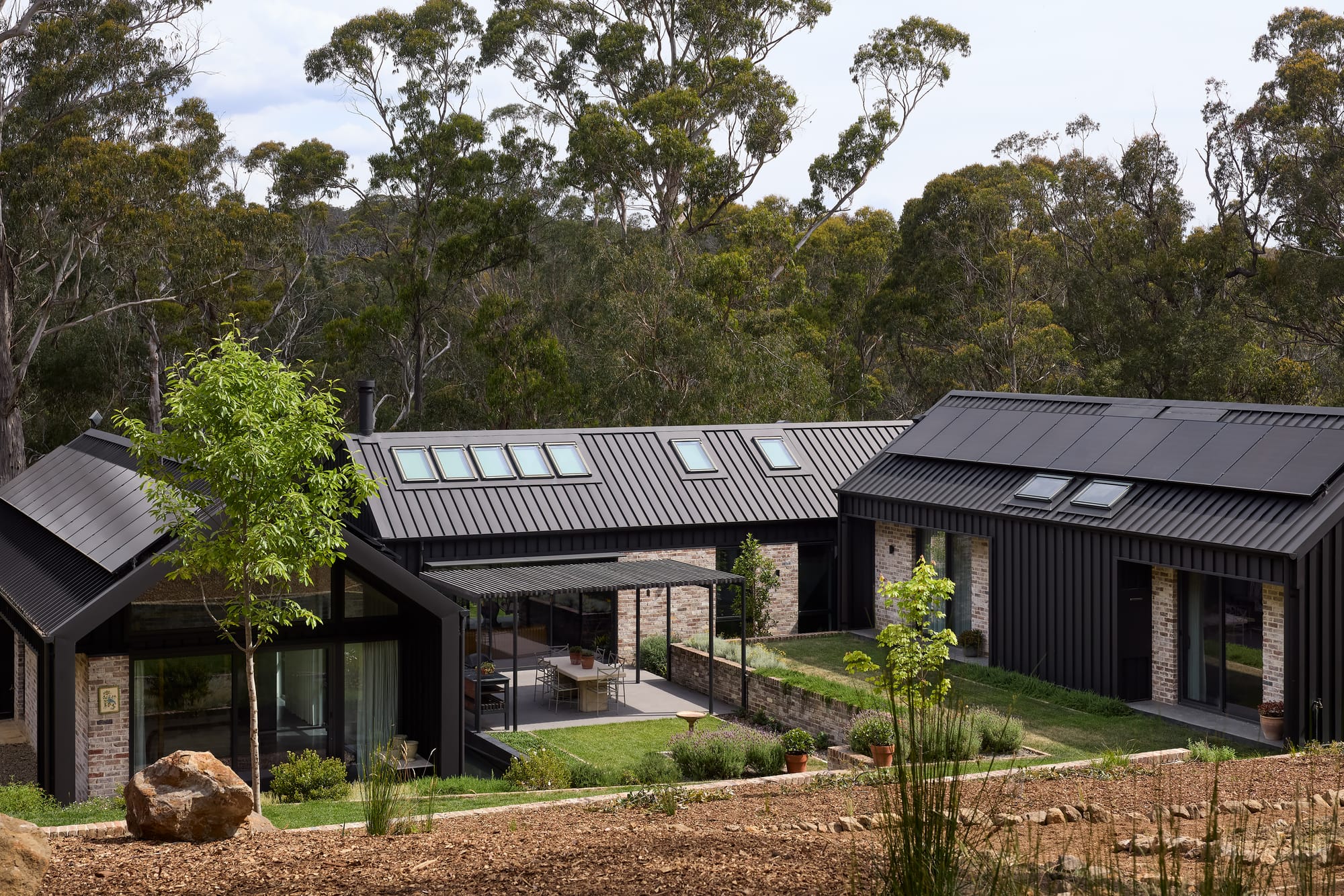 House Kimberley by AO Design Studio. Photography by Luc Remond. Aerial image of black clad home on tiered foundation with black clad exterior and grassed courtyards. 