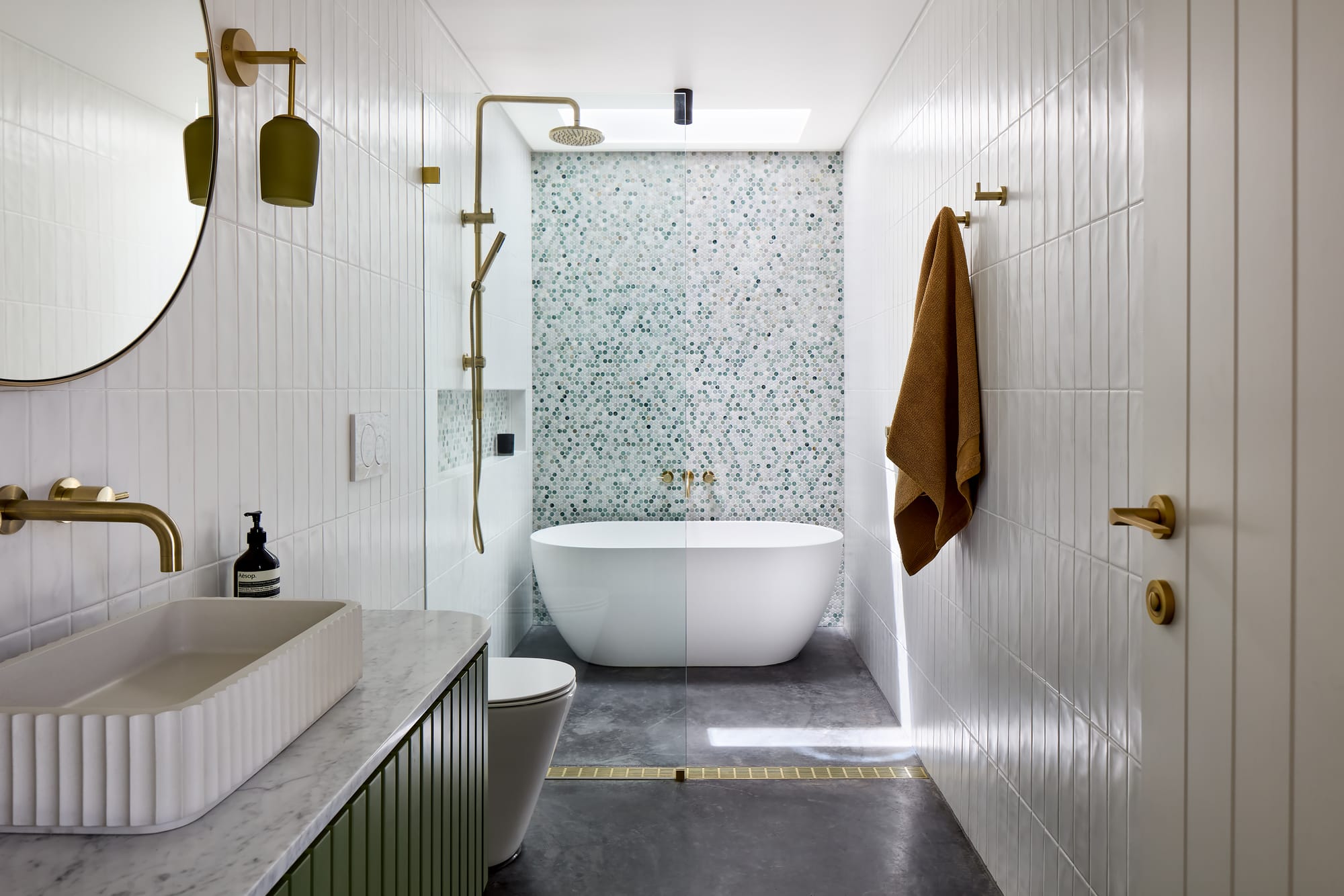 House Kimberley by AO Design Studio. Photography by Luc Remond. Bathroom with white wall tiles, blue and white mosaic tiles behind freestanding white tub and black floor tiles. 