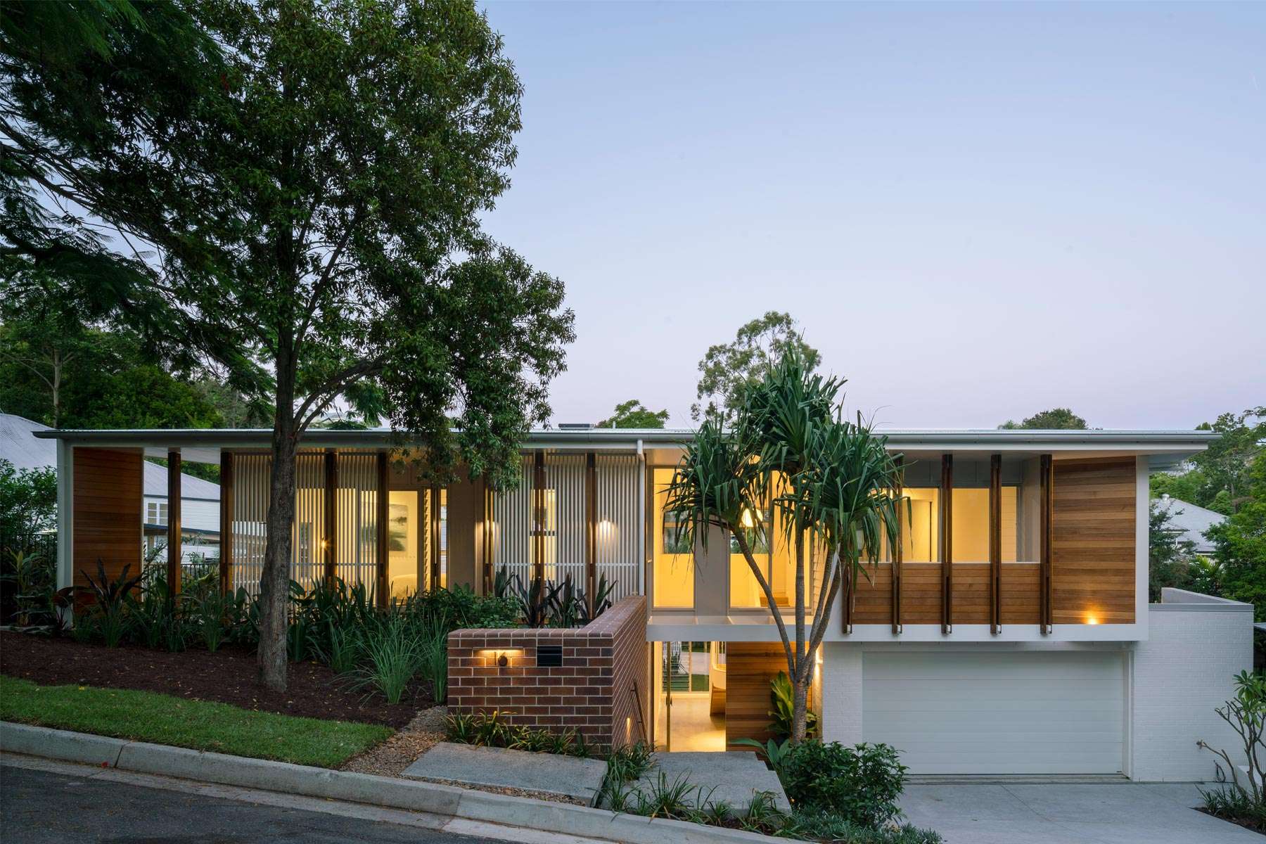 Auchenflower Courtyard House by Kelder Architects. Photography by Angus Martin Photography. Street facade of mid century modern two storey home with timber panlled upper floor, white sunken garage, brick feature wall and large windows and louvres across face.