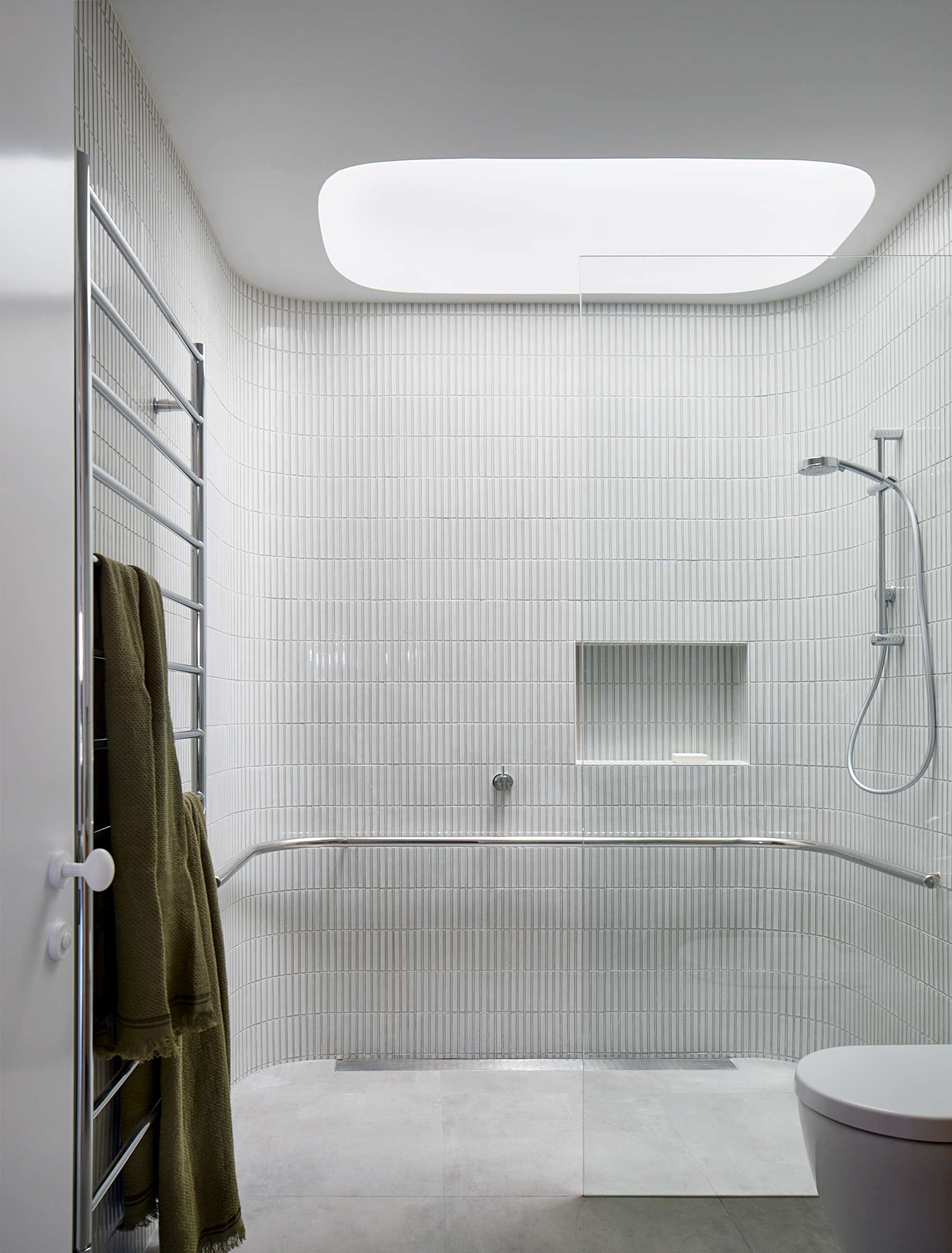 Envelop House by mcmahon and nerlich. Photography by Shannon McGrath. Bathroom with large curved wet area with finger tiles and steel hand rail, white floor tiles and a skylight.