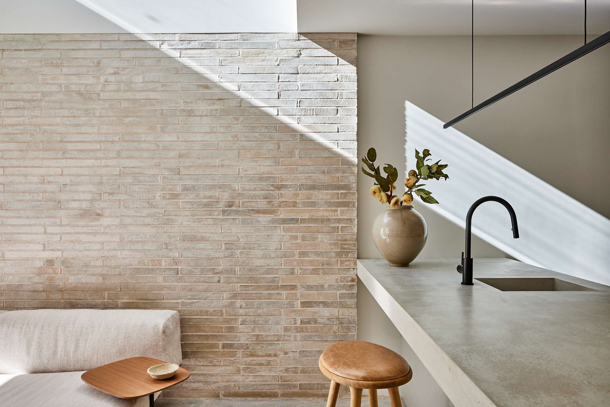 Crown Street Terrace by Studio Arkive. Photography by Pablo Veiga. kitchen and living room with concrete countertop, reclaimed blonde brick feature wall, beige couch, and brown leather stool.