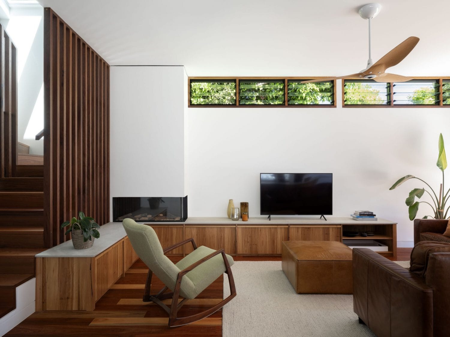 Surgo House by BIJL Architecture. Photography by Tom Ferguson. Living room with timber flooring, cabinetry and vertical screening, a green mid-century modern rocking chair and a brown leather couch.