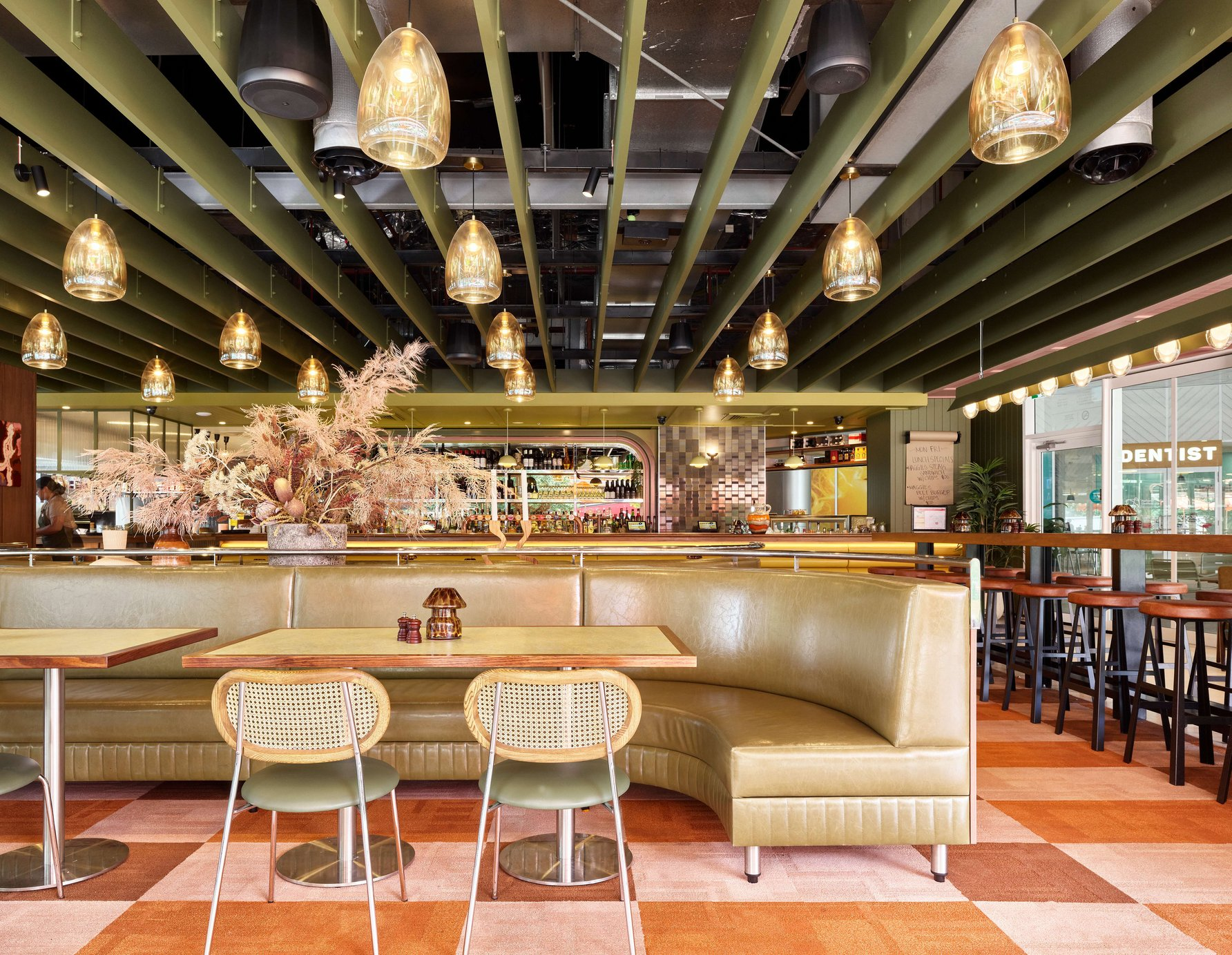 Maggie May Supper Club by BSPN Architecture. Photography by Scott Burrows. Hospitality space with pink and orange checkered carpet, olive leather curved booth seating and glass lanterns. 