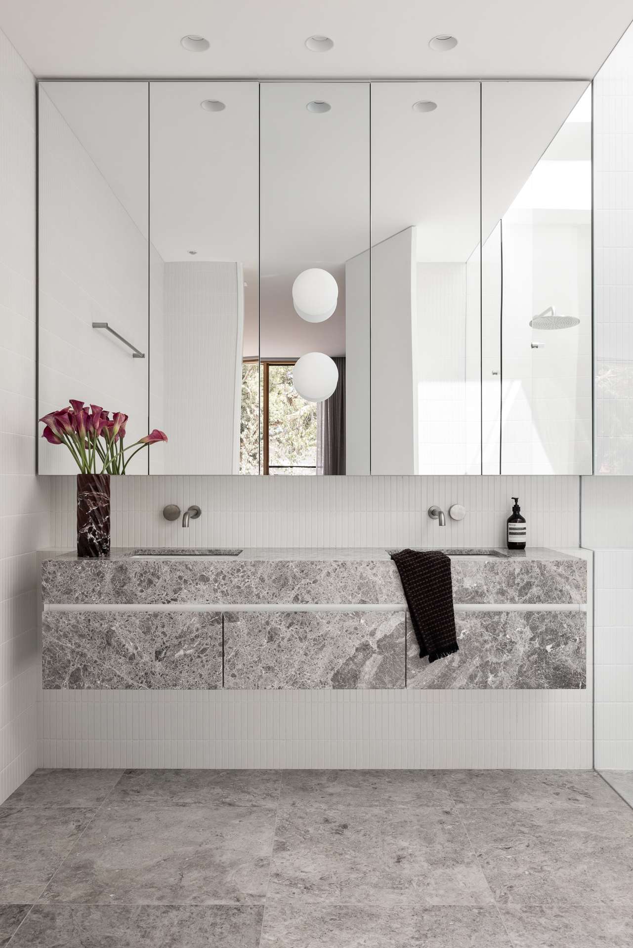 Bastings House by FURNISHD. Photography by Dylan James. Bathroom with marbled grey floating vanity, grey tiled floors, white finger tiled walls and a large vanity mirror.