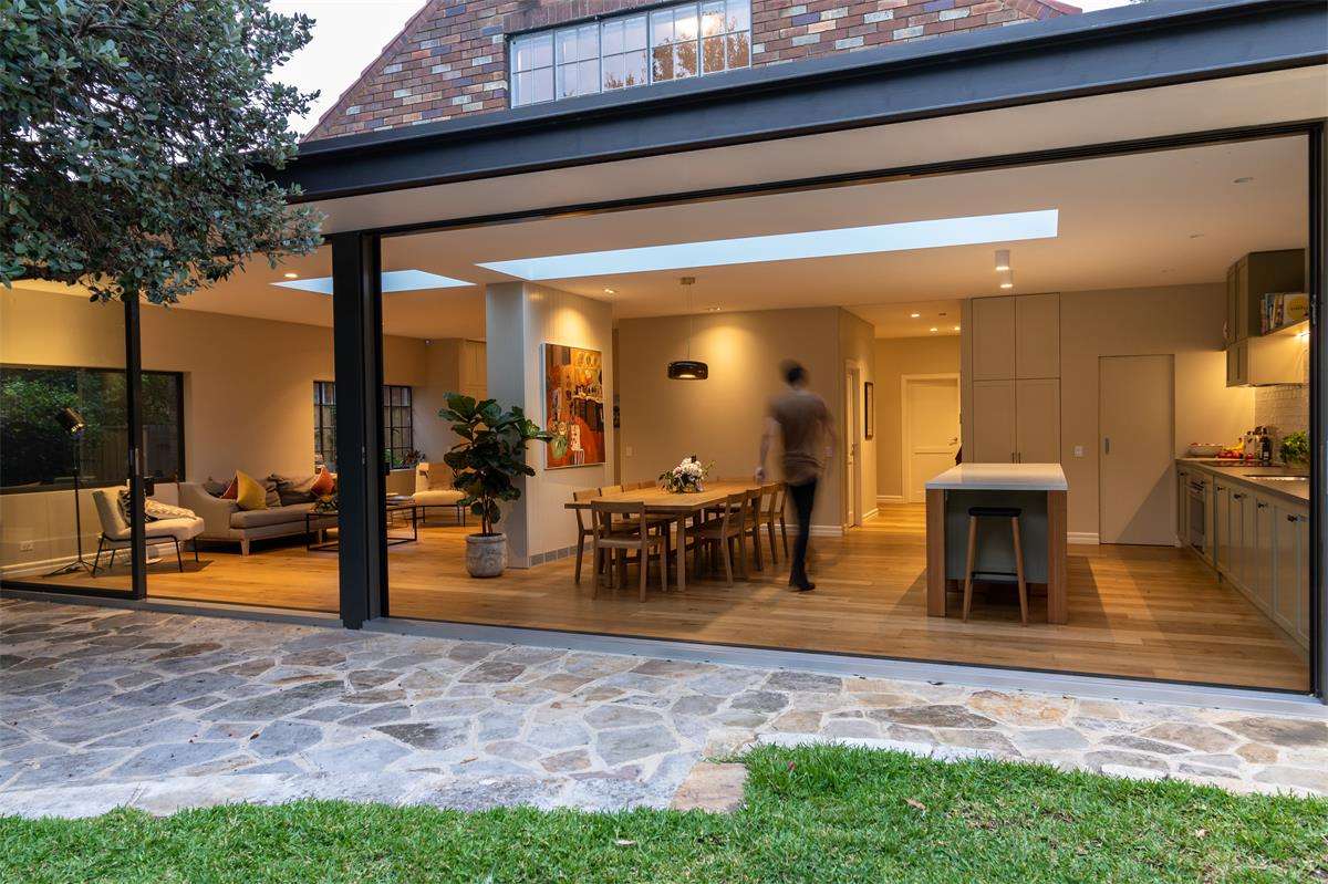 Gable End by Castlepeake Architects. Photography by Jason Waddell. Open plan kitchen, living and dining space running along the rear facade of a residential property, opening onto a paved and grassed backyard through full height sliding doors the full length of the home.