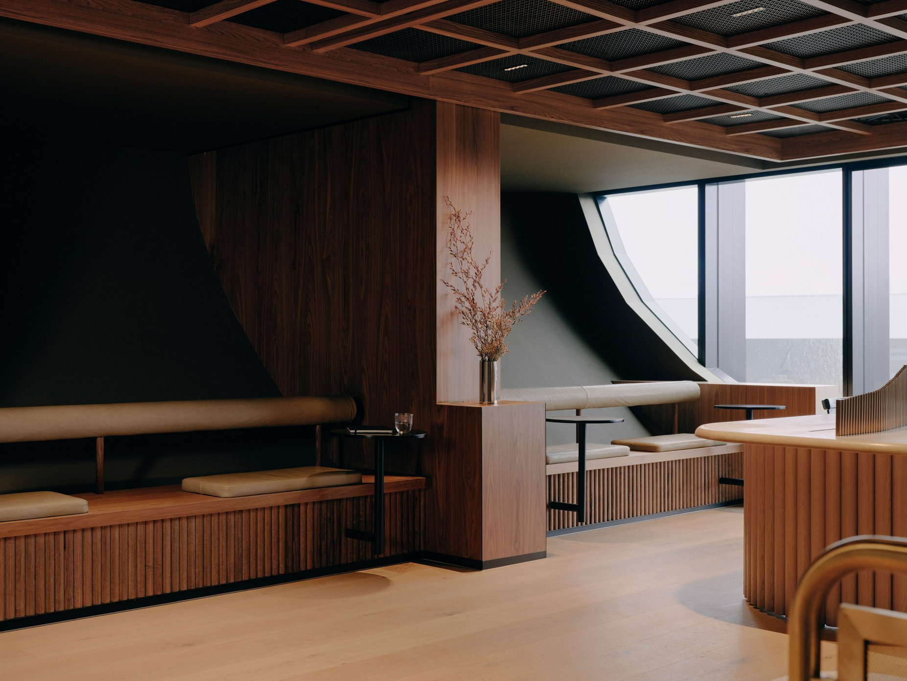 Aerofoil Workspace Melbourne Airport by FK. Photography by Tom Ross. Workspace with integrated leather and fluted timber bench seats, dark green curved walls and a large circular window.