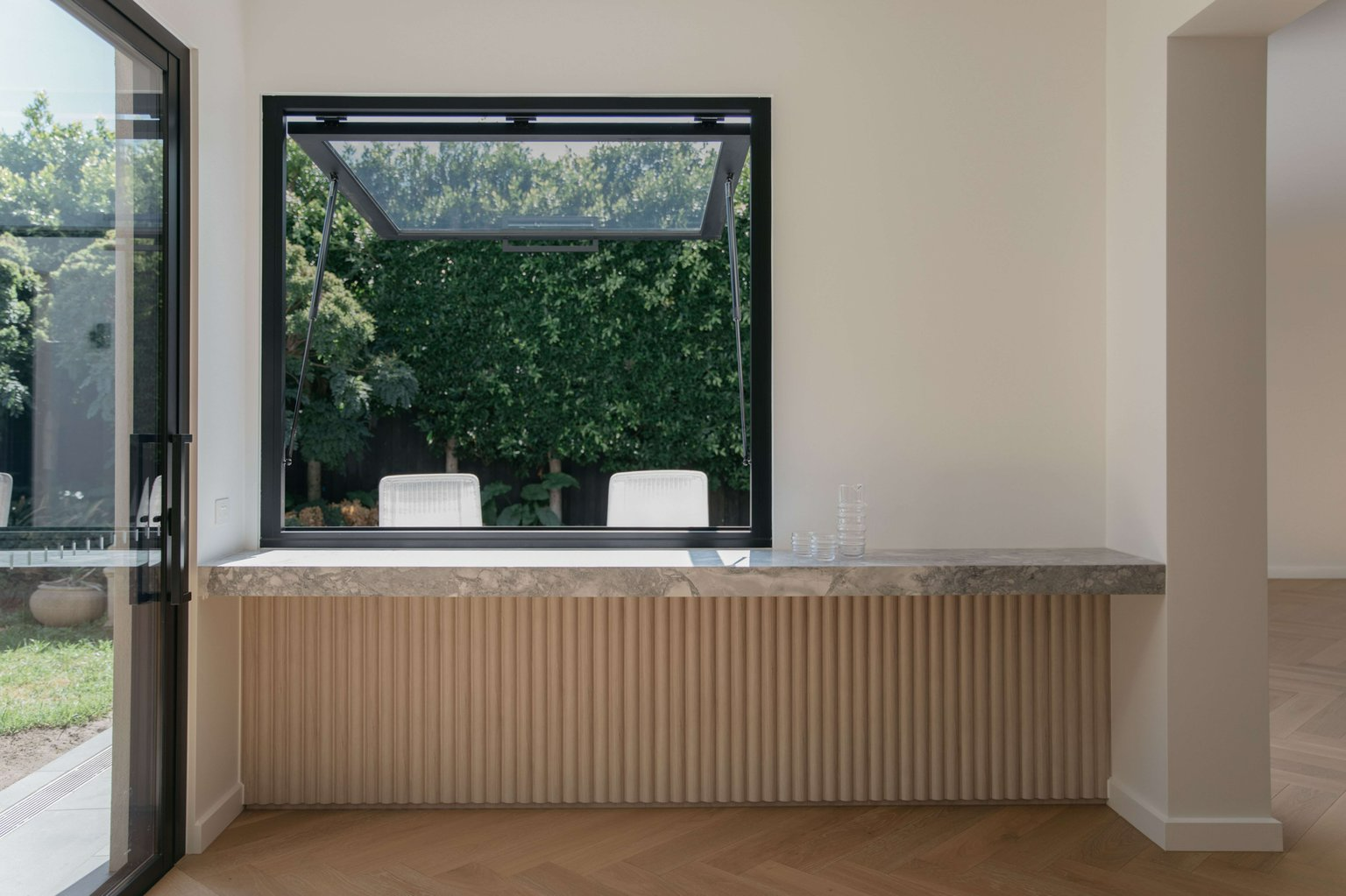 Little Moffat by Merrylees Architecture. Photography by Siy Studio. Large window connecting interior floating marble bench with garden and seating outside.