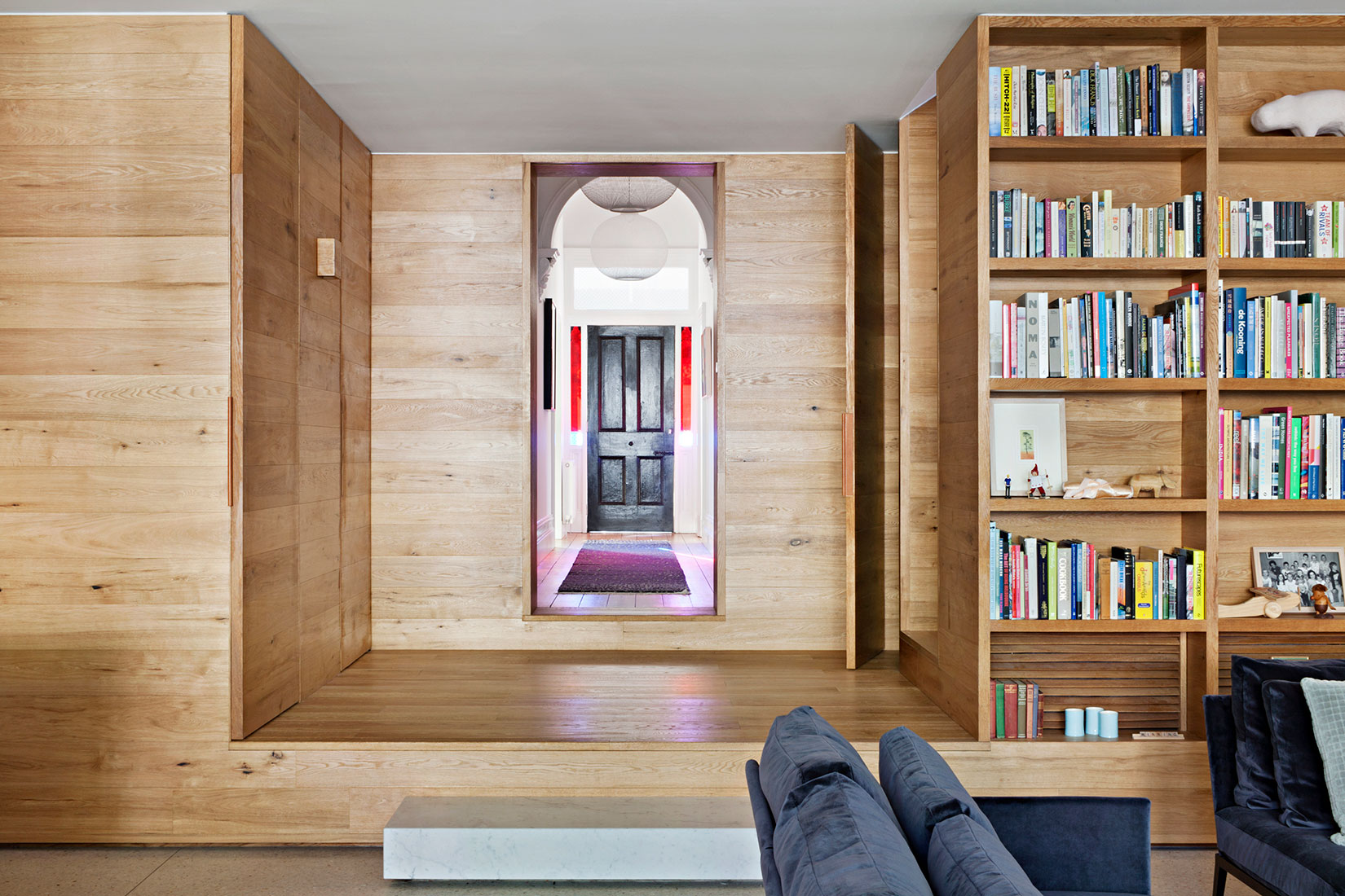 Victoria Gardens House by Lucy Clemenger Architects. Living room with entrance view featuring oak wood, frame and shelving installation.