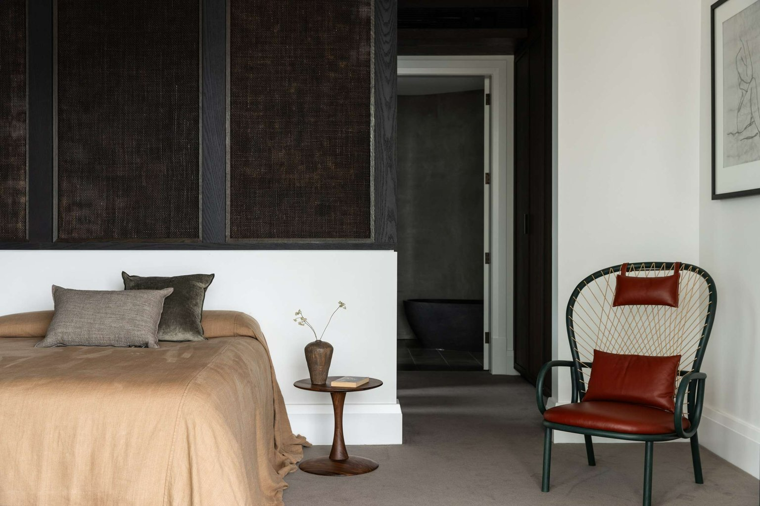 Ripple House by Marker Architecture. Photography by Simon Whitbread. Bedroom with dark woven wall texture, beige bed covers, a armchair with red leather cushions and grey carpet.