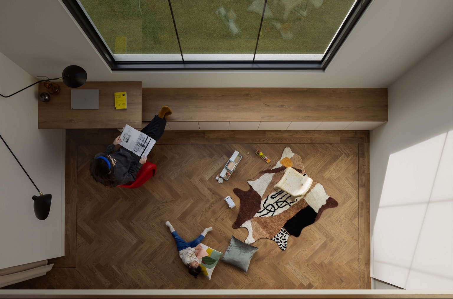 Terracotta House by R Architecture. Photography by Matt C. Birds eye view of living/office space with herringbone timber flooring, a timber window seat and desk and a large window looking onto a grassed backyard.
