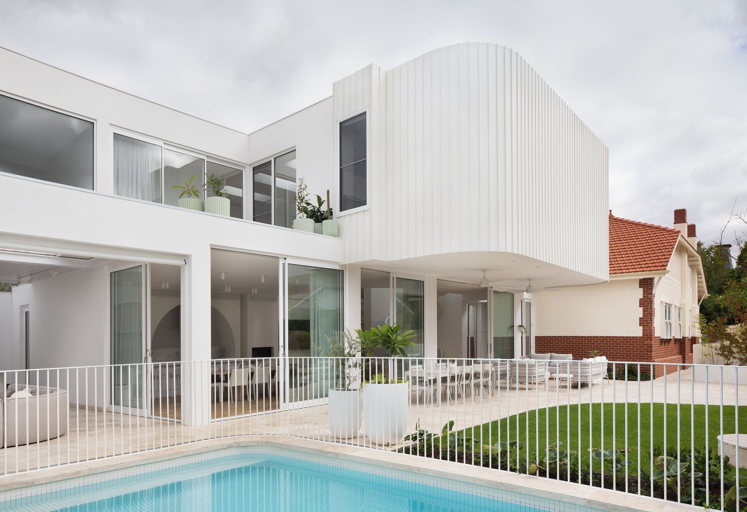 The Grove by Taouk Architects. Photography by Emily Bartlett. ReR FACADE, Grden and pool of double storey residential home with large rounded overhand finished in white clad.