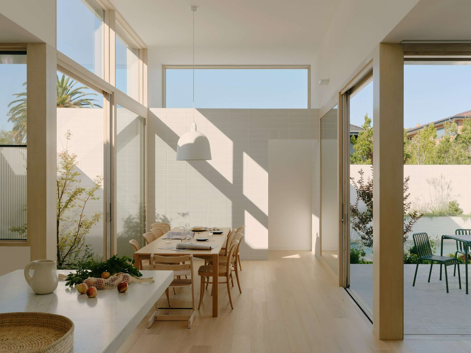 Wheatland House by Tom Robertson Architects. Photography by Tom Ross. Open plan living and dining space with high ceilings, full height windows, timber flooring and neutral furnishings opening up to paved patio on the left through sliding glass doors.
