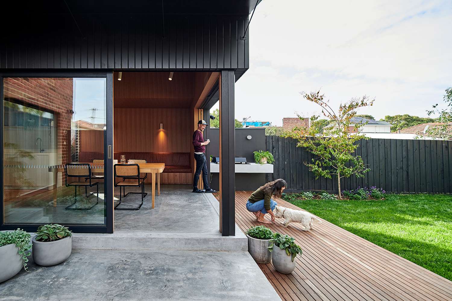 Thornbury Residence by True Story. Photography by Dean Bradley Photography. Full height black framed sliding doors opening to connect interior dining space with exterior patio, timber deck and grassed backyard.
