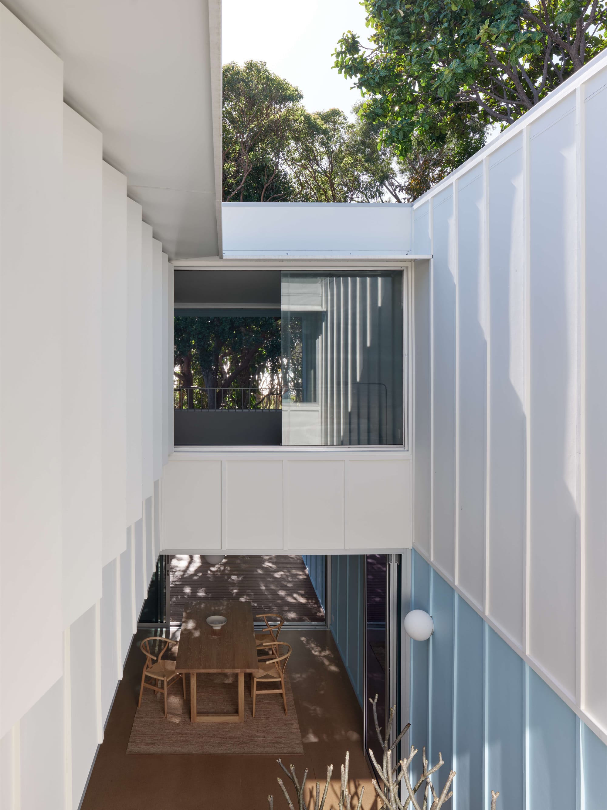 Blok Peregian by Blok Three Sisters. Photography by Christopher Frederick Jones. Second storey of home with full height open-air courtyard void, looking down to dining room with timber floor and dining table.