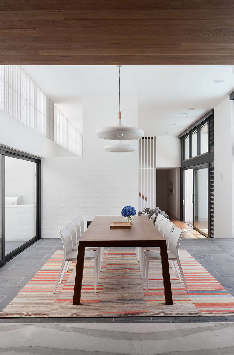 Stepping House by Bower Architecture & Interiors. Photography by Shannon McGrath. Double height dining space with white brick walls, patterned rub and grey slate flooring.